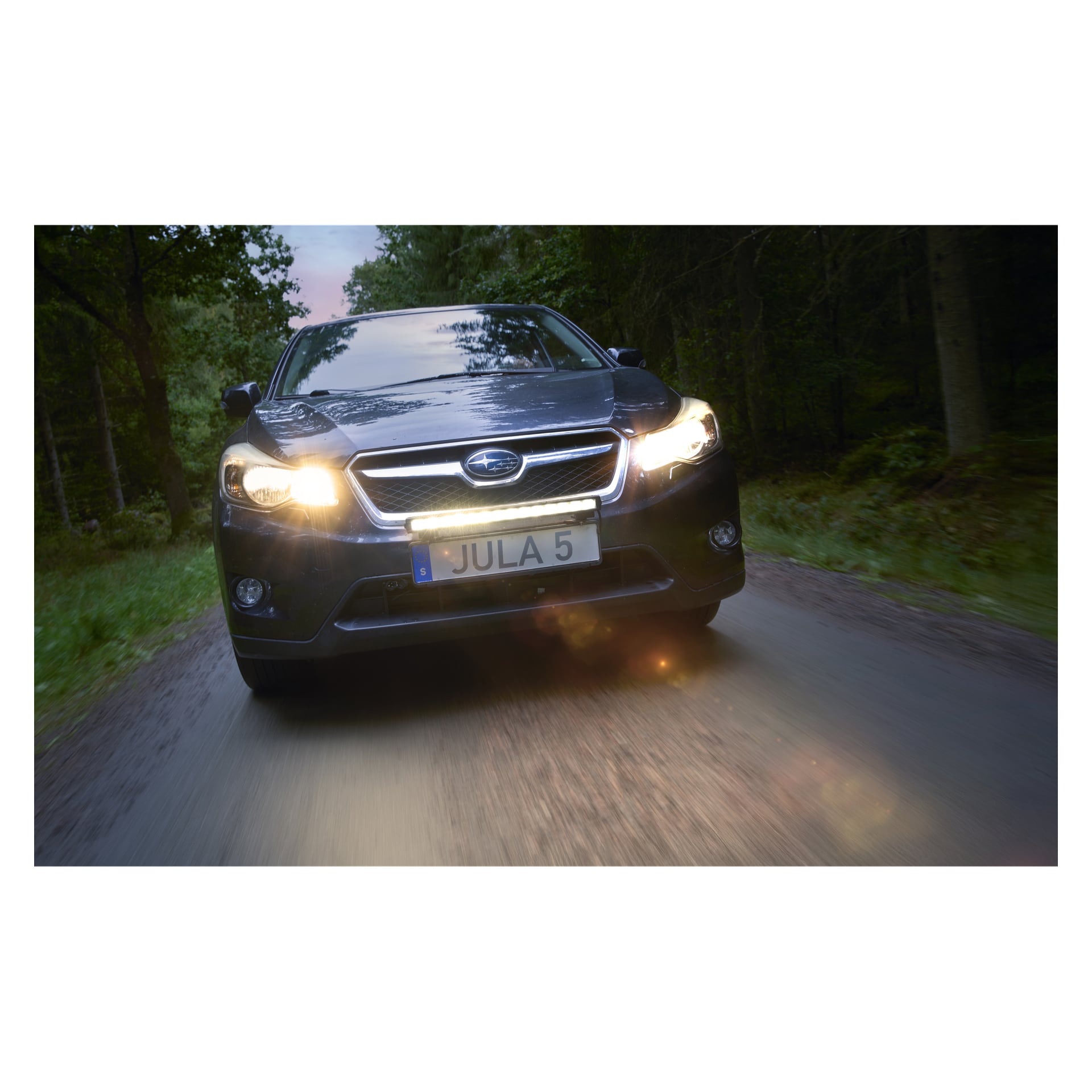 En Subaru med en Hamron Light bar LED kör genom en skog, strålkastarna på. Framsidan markerar skylten JULA 5.