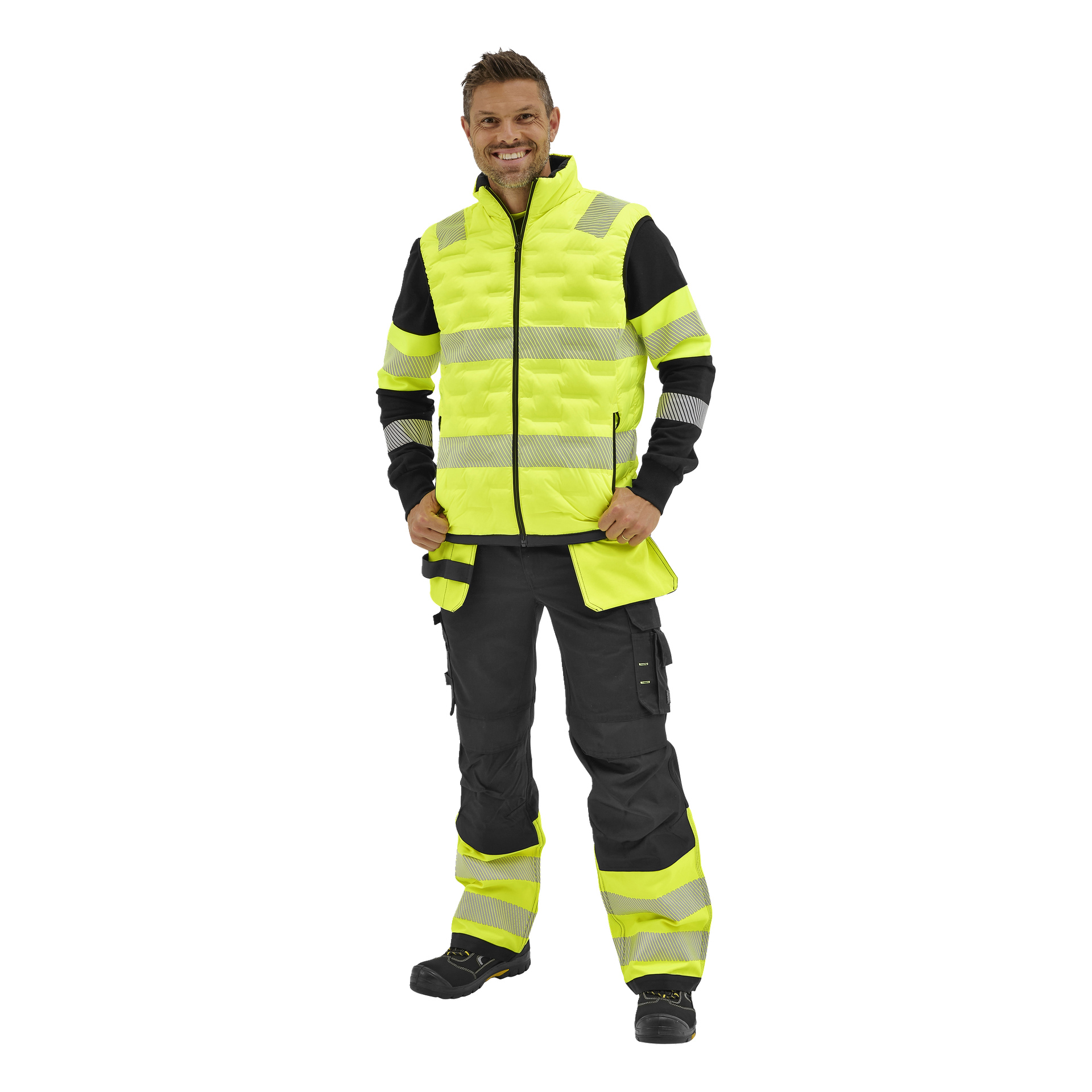 Leende man i en gul och svart högsynlig väst, reflekterande cargobyxor, svart långärmad tröja och arbetsskor.