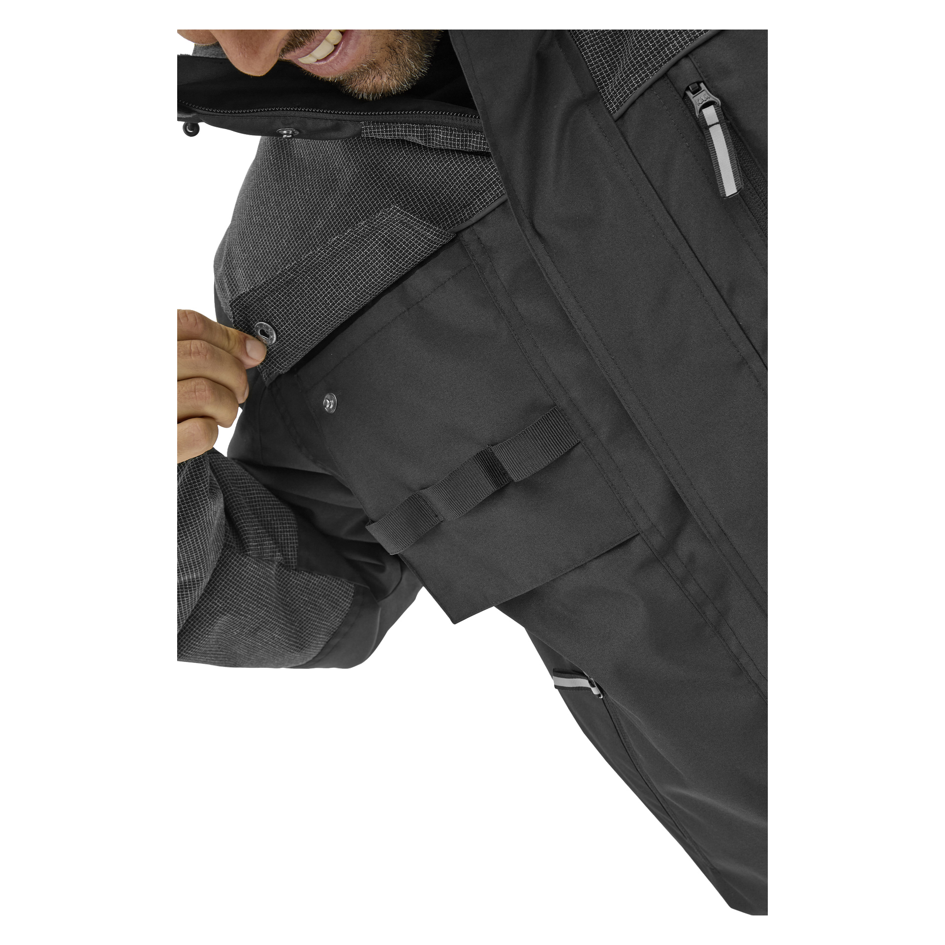 En person i en mörkgrå Bluewear Johan arbetsjacka knäpper krageknappen. Jackan har bröst- och klafffickor samt texturerade ärmar.