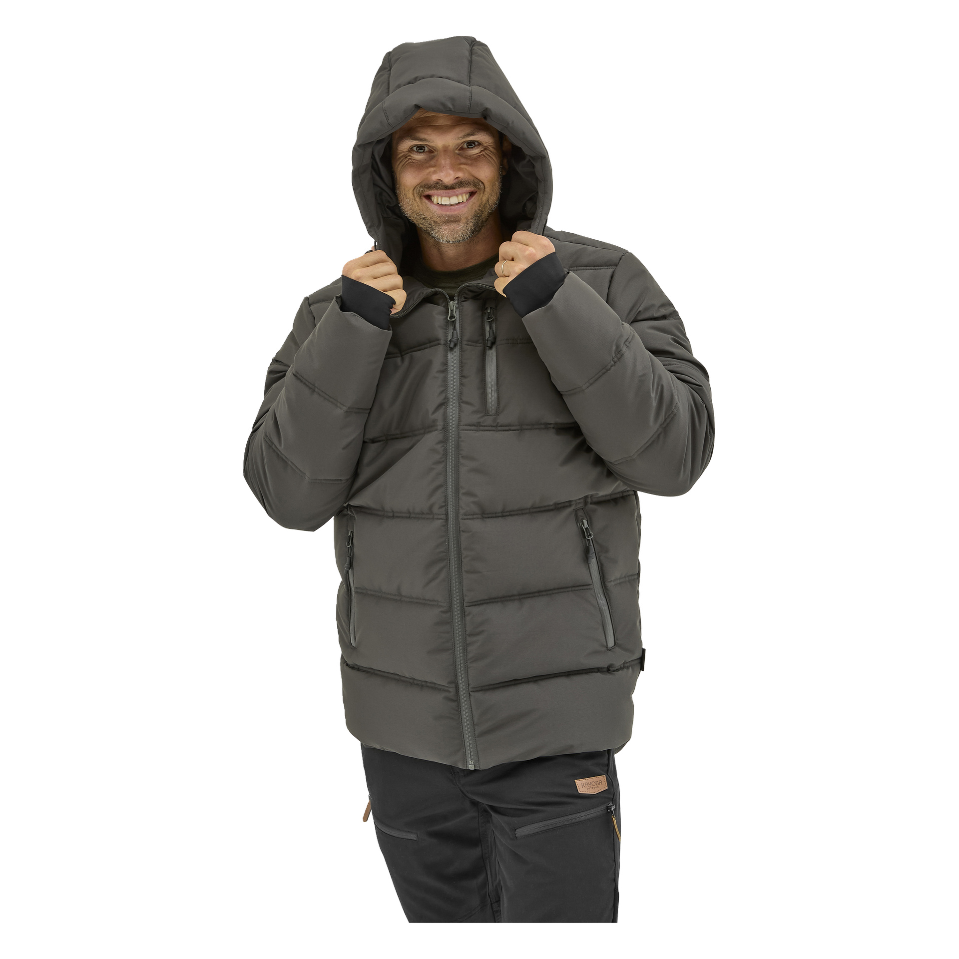 Henkilö katsoo eteenpäin, hymyillen ja pitäen "Kayoba Outdoor Men's winter jacket Sveg" -takin huppua. Harmaassa pallotakissa on useita vetoketjullisia taskuja, vaakasuoria ompeleita ja sitä käytetään tummien housujen kanssa.