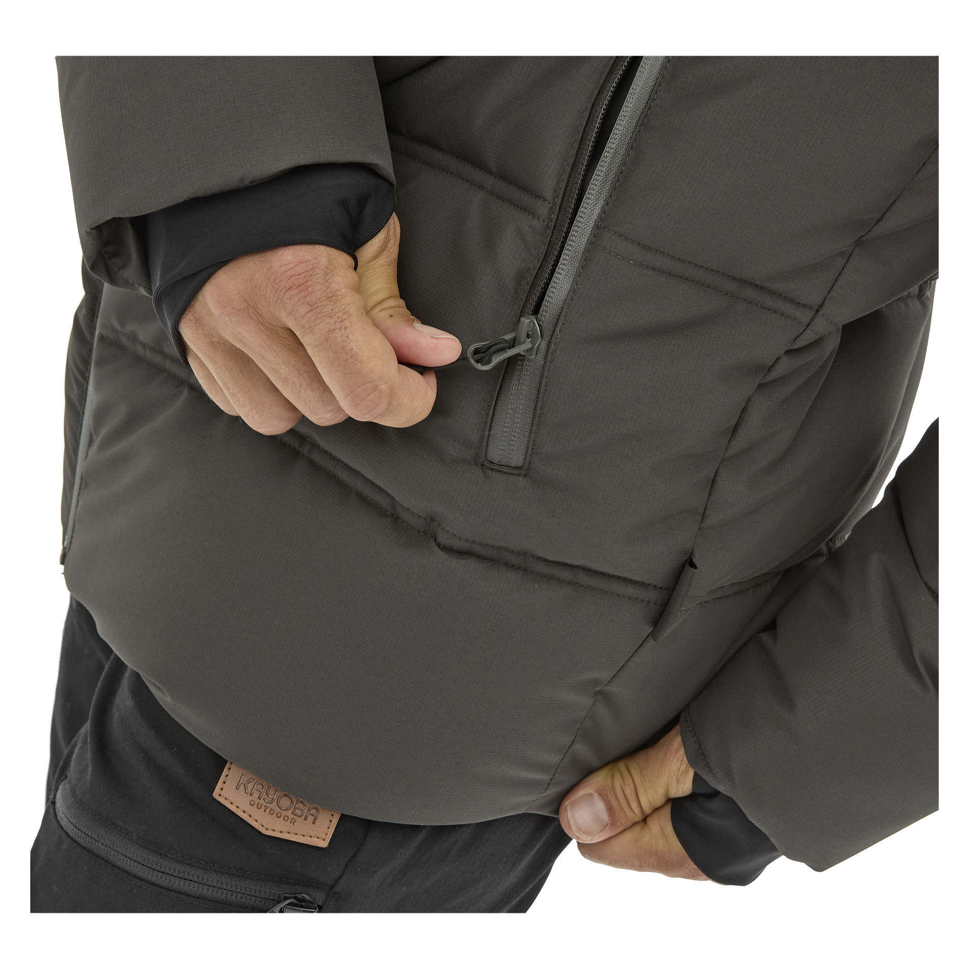 Henkilö, joka on pukeutunut Kayoba Outdoor Men's talvitakki Svegiin, tummanharmaaseen ja mustiin housuihin, nähdään avaamassa takin pystysuoraa rintataskua. Kuva keskittyy tarkasti heidän käsiinsä, jotka ovat vuorovaikutuksessa takin kanssa.