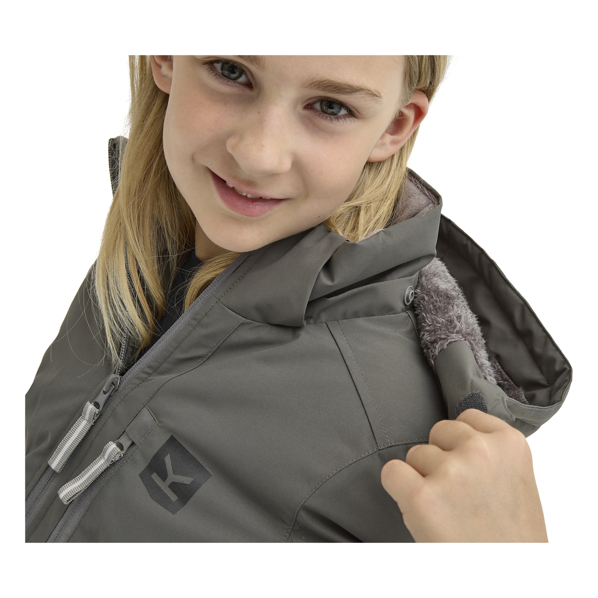 En ung flicka med långt blont hår bär "Kayoba Outdoor Children's winter jacket Kläppen", en grå huvajacka, drar i kragen och ler mot kameran.
