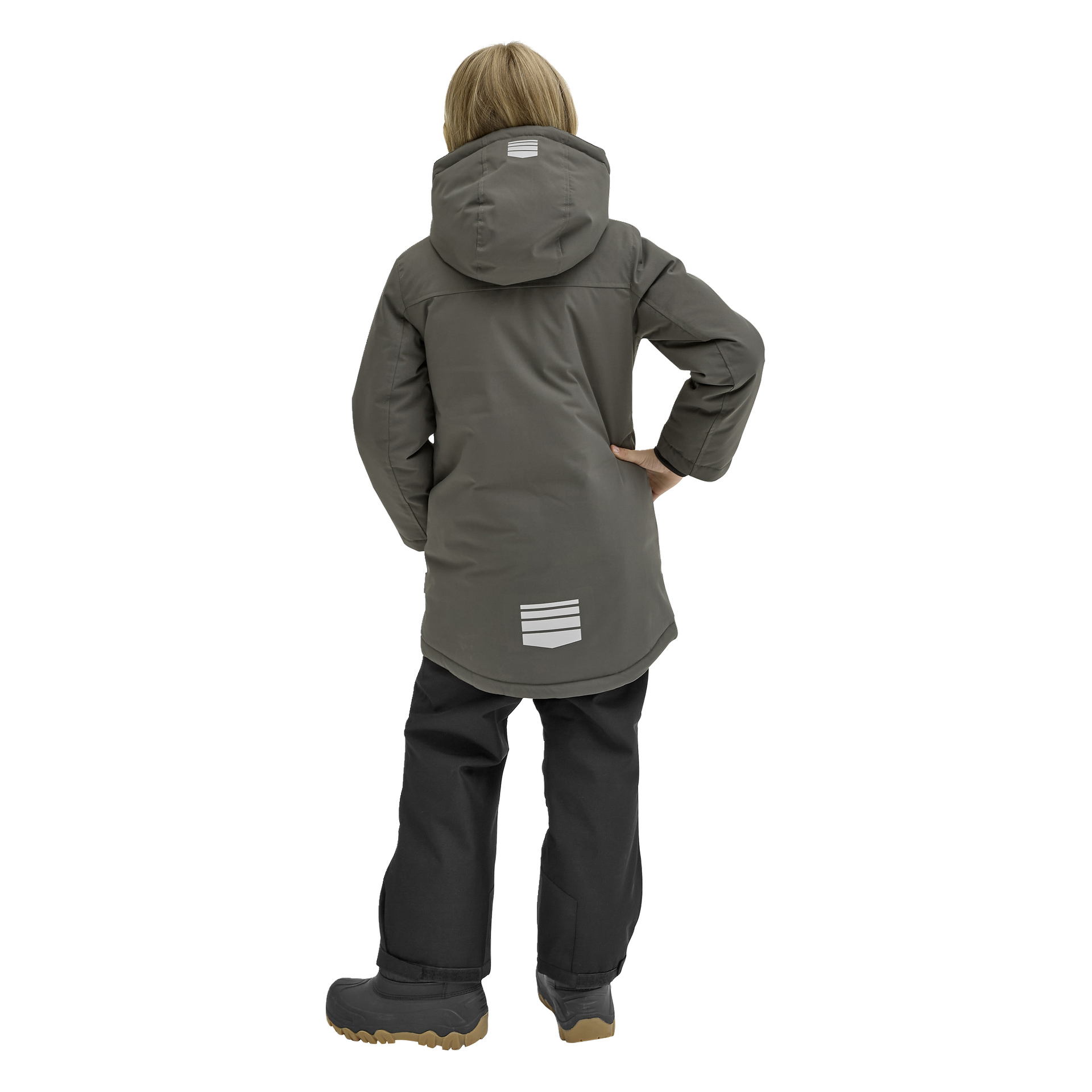 Ett barn i en grå Kayoba Outdoor Children's vinterjacka "Kläppen" med reflekterande ränder på ryggen och svarta snöbyxor står vänd bort, ena handen vilande på höften, och bär vinterstövlar med beige sulor.