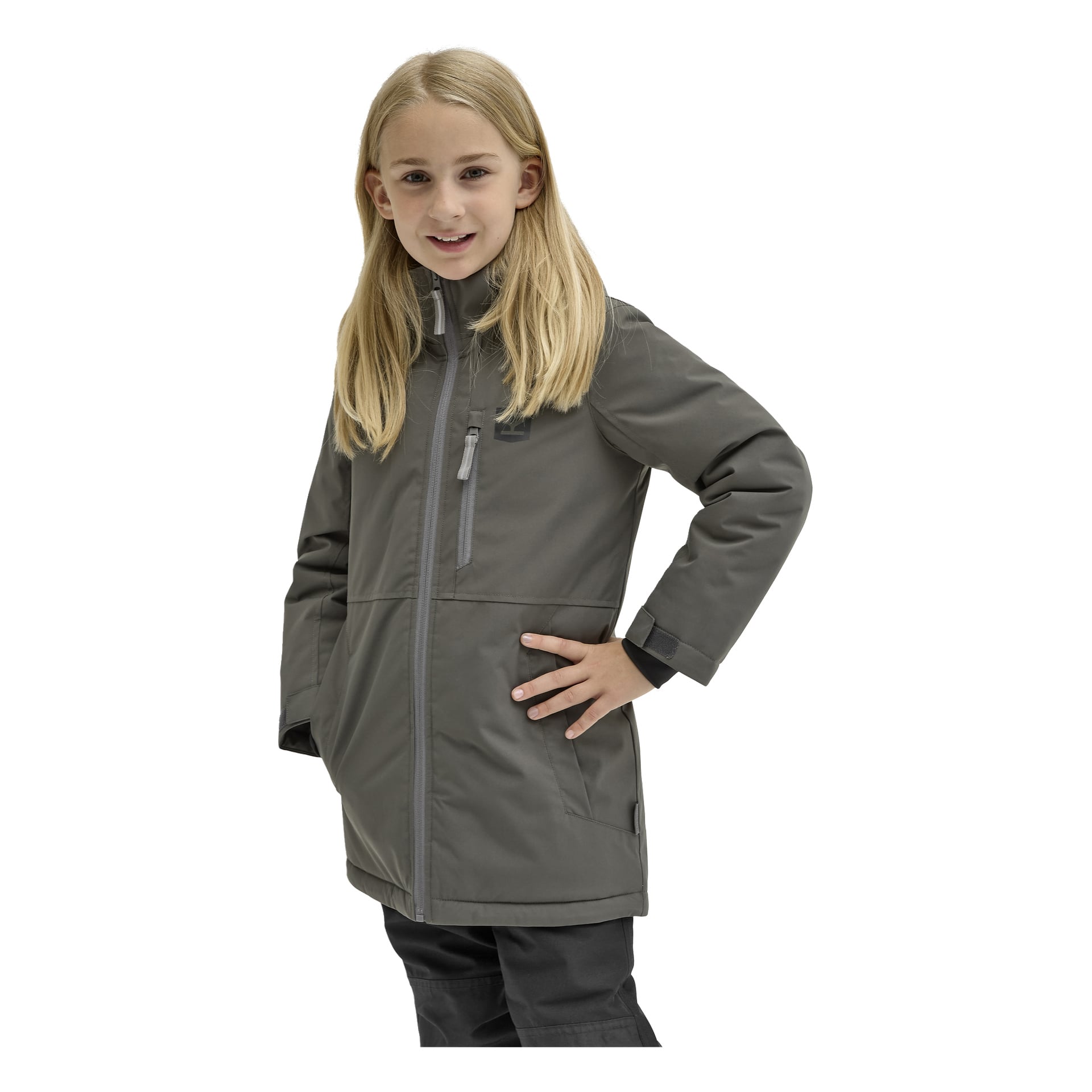 Ett barn med långt blont hår bär Kayoba Outdoor Children's vinterjacka Kläppen, beskriven som en "grå dragkedja med hög krage," tillsammans med svarta byxor. Barnet står självsäkert, med ena handen på höften, och ler mot kameran.
