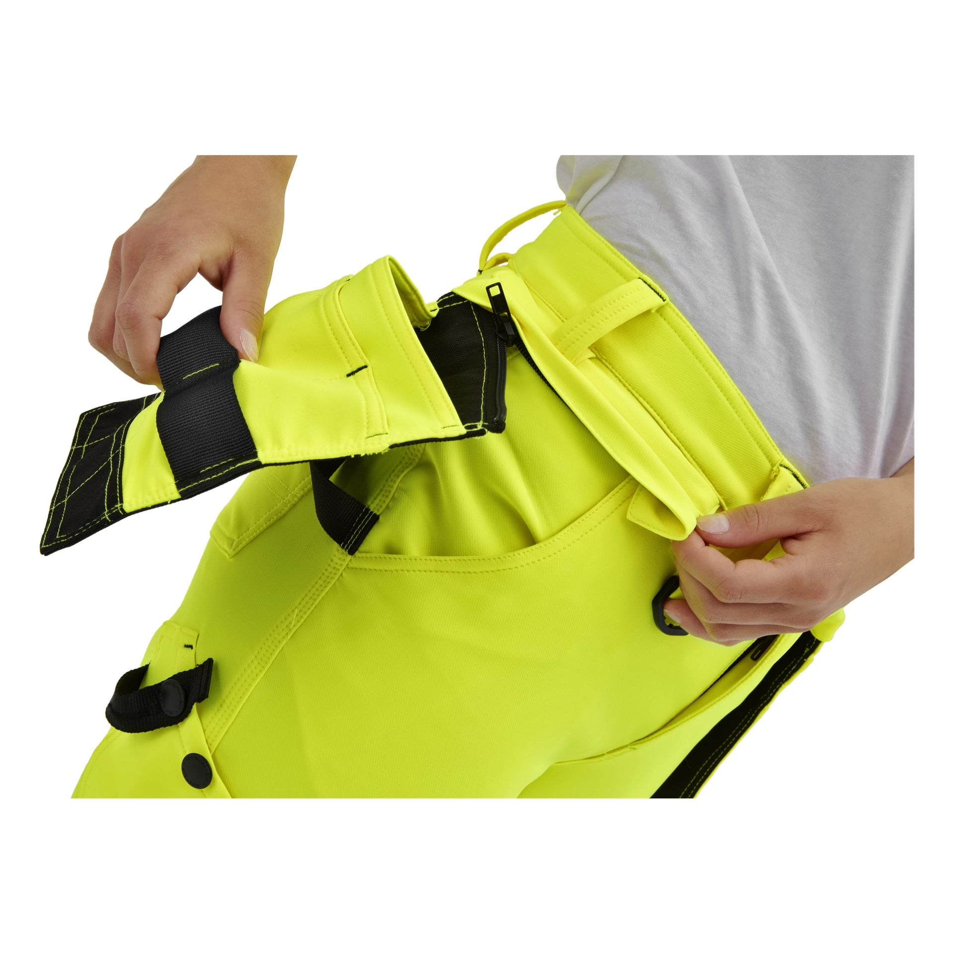 En person i klargula Bluewear Pro Workwear Dambyxor från Stella fäster en svart och gul kardborreband, iklädd en vit skjorta.