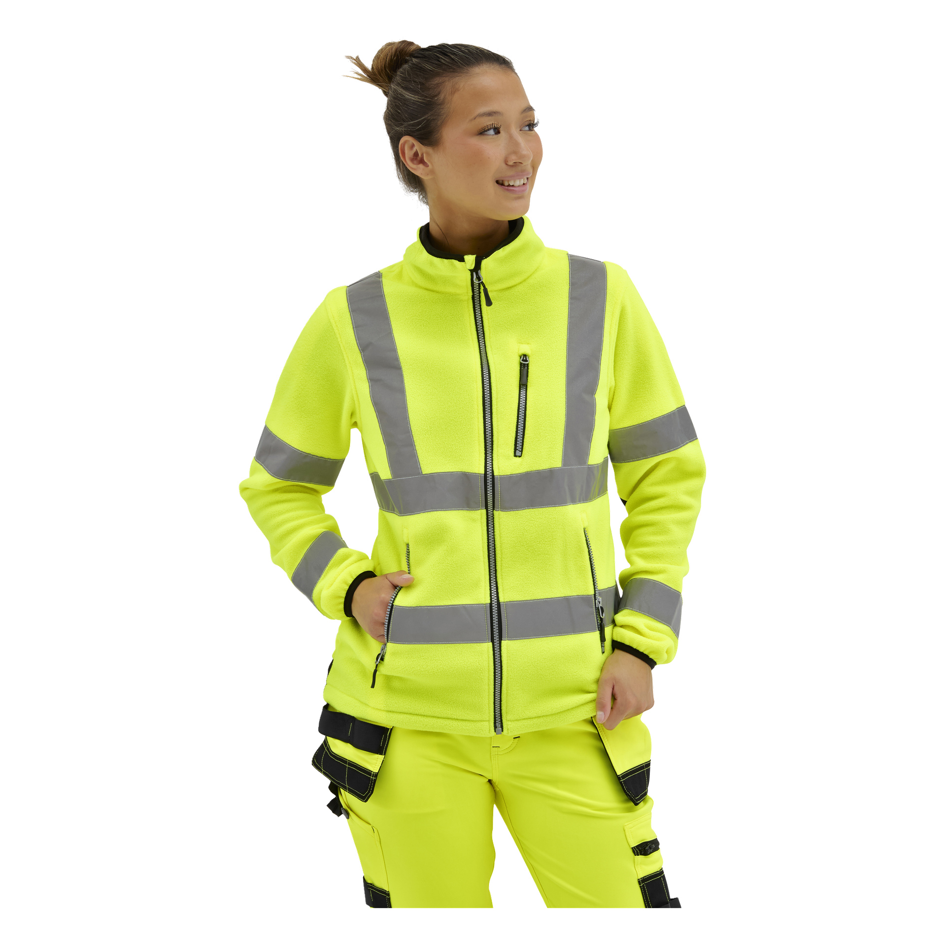 En kvinna i en ljusgul hi-vis fleecejacka med grå reflekterande ränder och fickor, samt matchande arbetsbyxor, står på sidan.