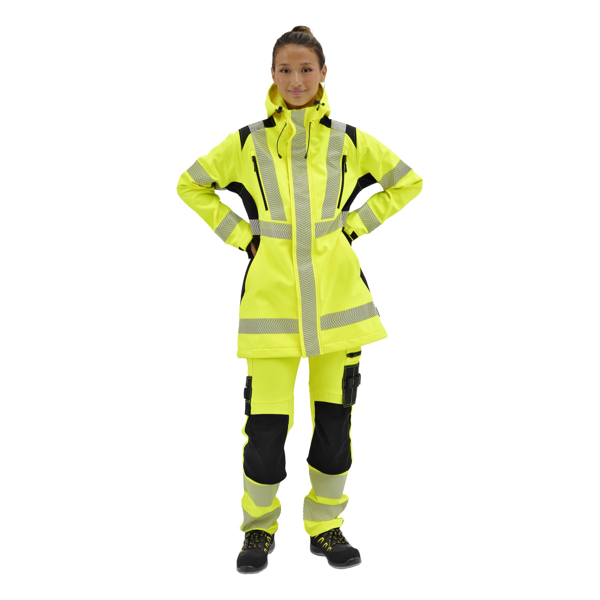 En person står med händerna på höfterna i en Bluewear Hi-Vis Merrit-jacka, matchande byxor och svarta skyddsskor.