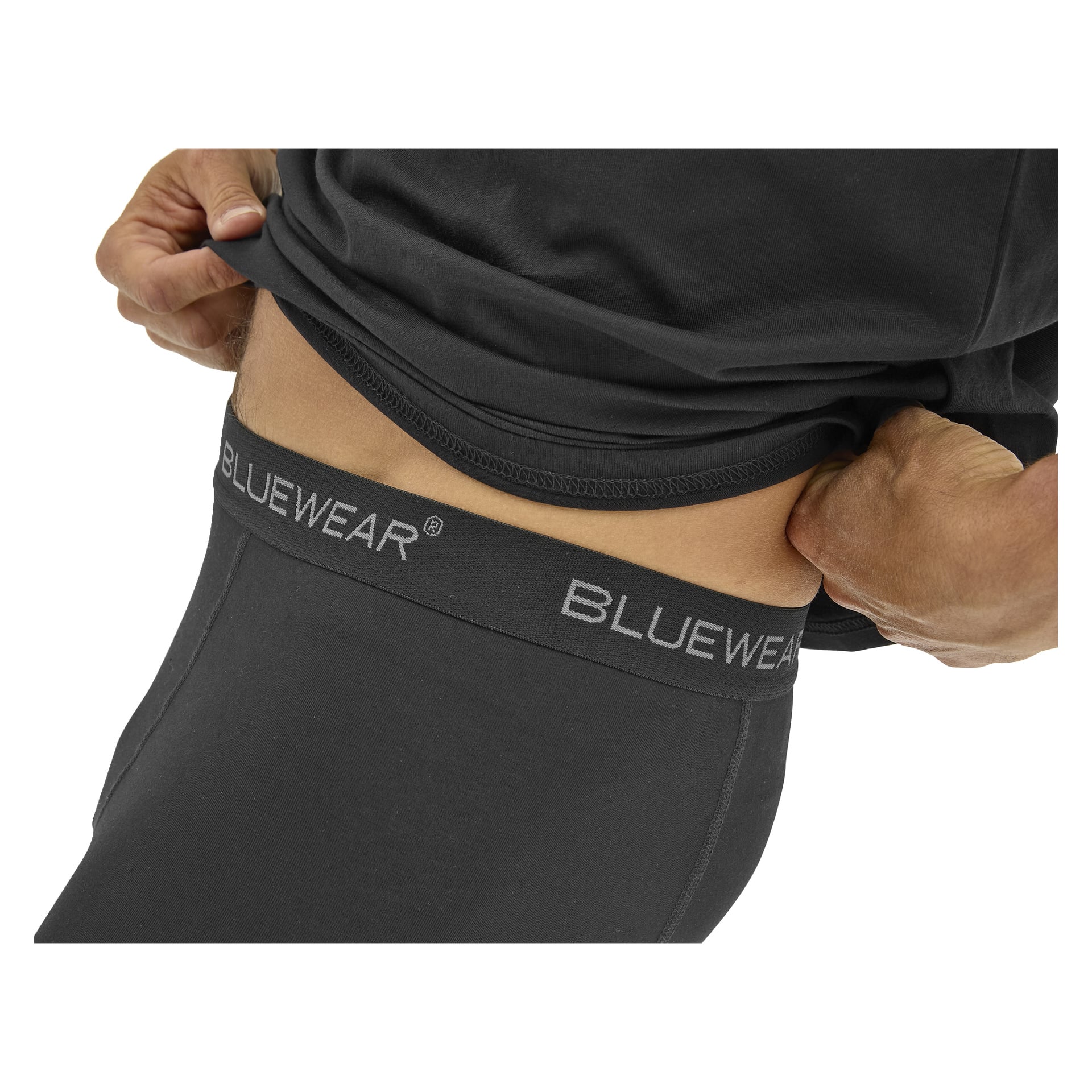 En person lyfter en svart skjorta och blottar midjebandet på svarta byxor eller underkläder märkt BLUEWEAR. Fokus ligger på midjebandet.