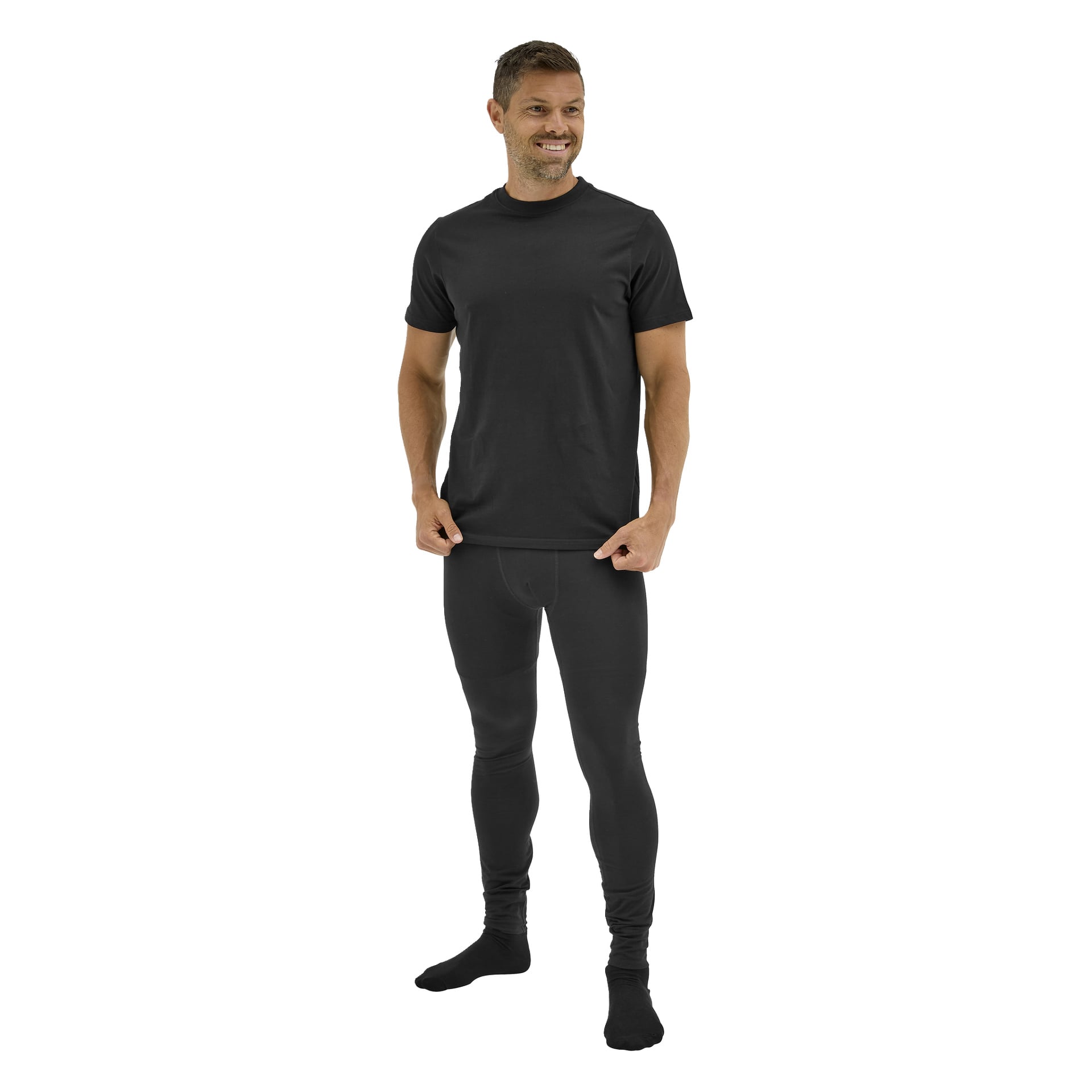 En man ler framåt, håller i sin skjortkant, klädd i Bluewear Long Johns Gnejs svarta leggings, T-shirt och strumpor.
