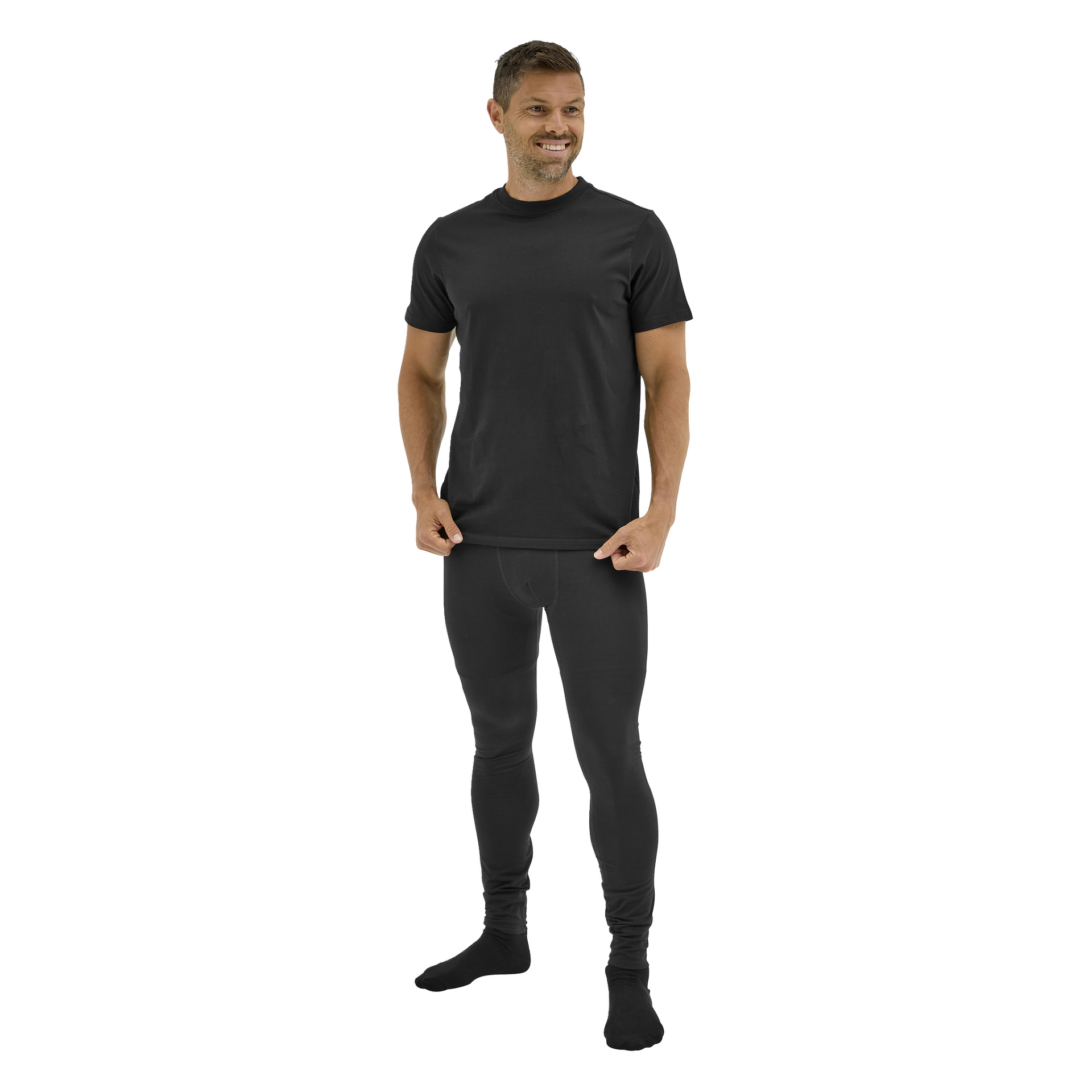 En barfota man står på sidan, leende, i en åtsittande svart Bluewear Long Johns Gnejs-skjorta och matchande leggings, håller i sin skjortfåll.
