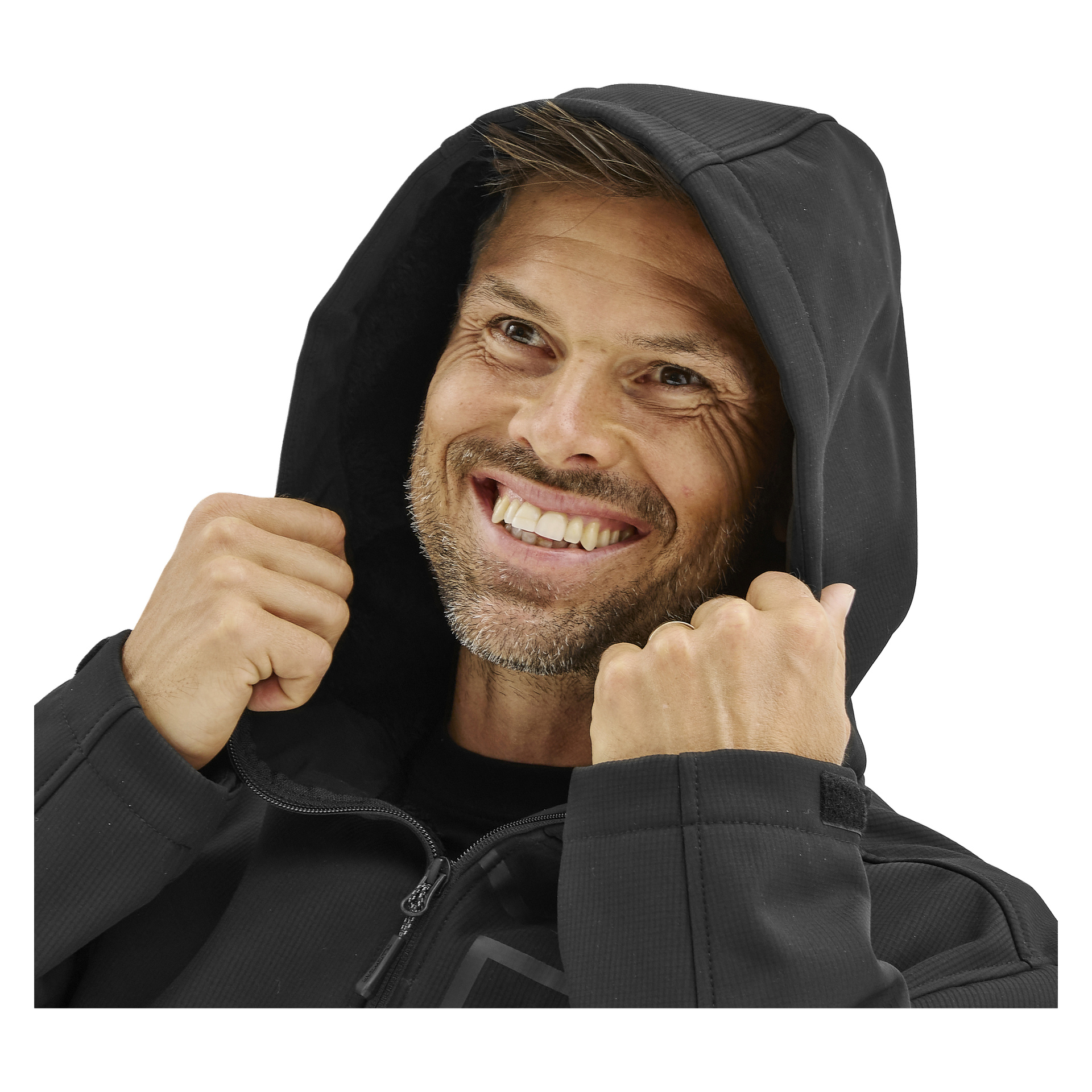 En leende man med ljus hy, kort brunt hår och stubb håller huvan på en Bluewear Men's Gustaf softshelljacka.