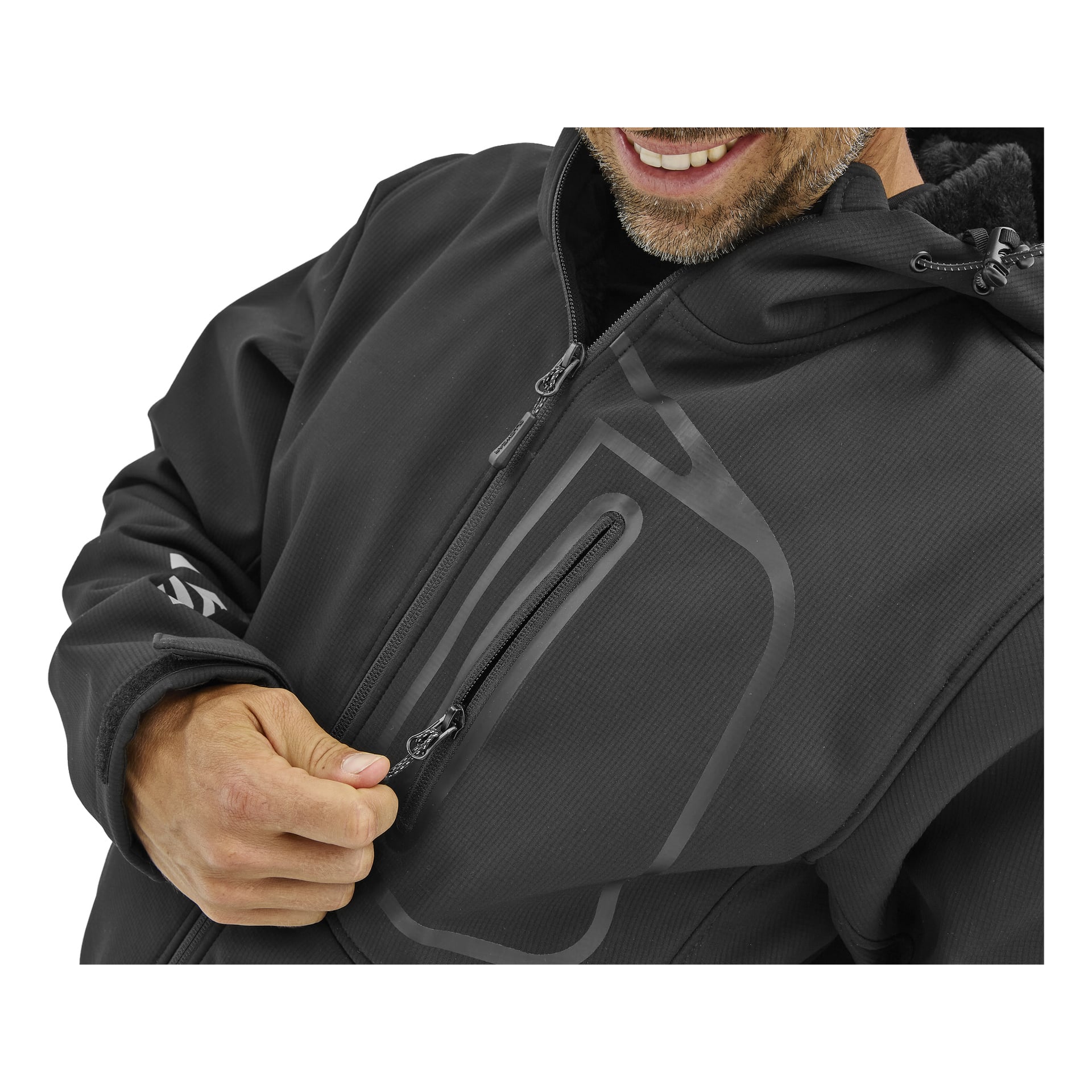 En man ler medan han drar ner dragkedjan på bröstfickan på en svart Bluewear Gustaf softshelljacka, hans korta skägg delvis synligt.