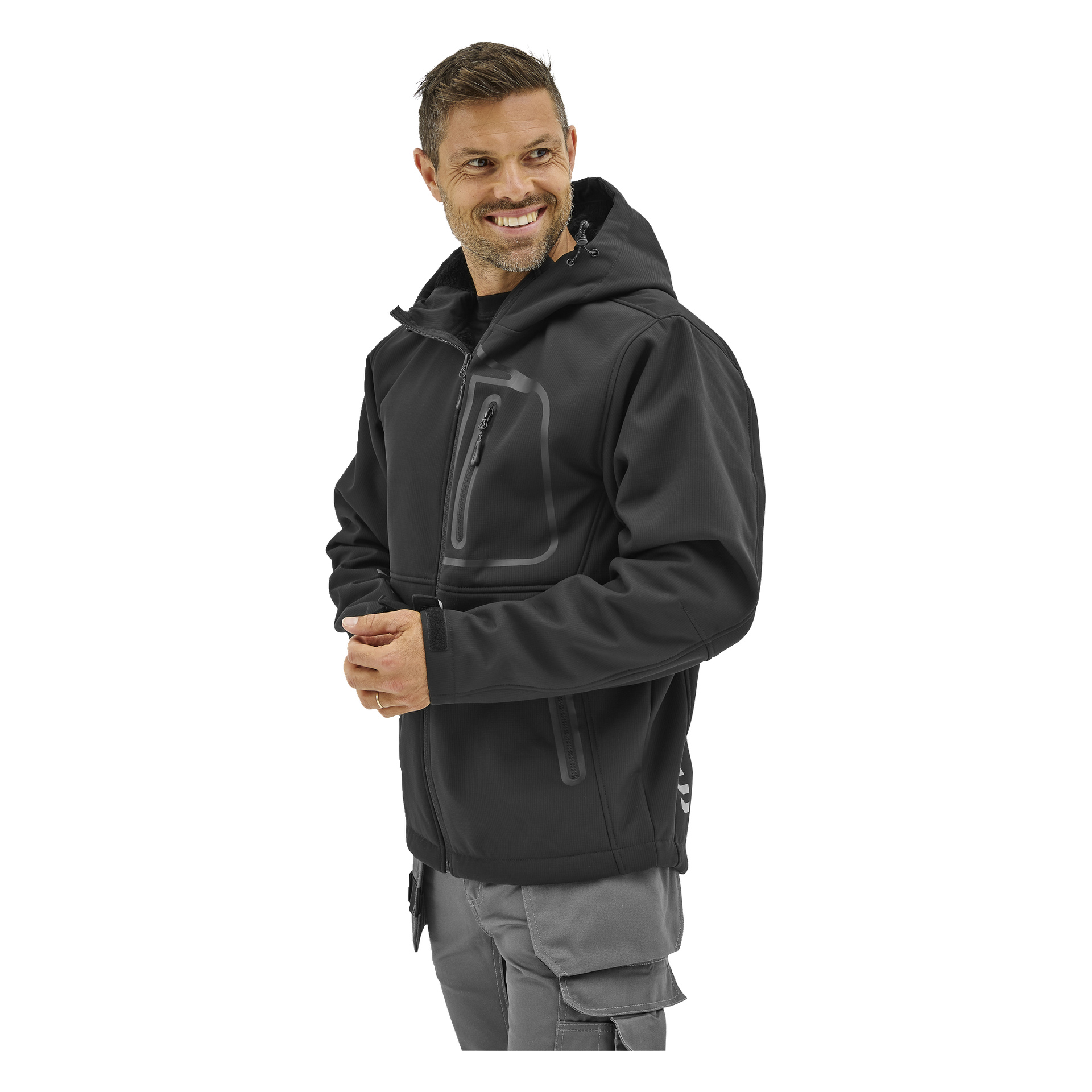 En man i en Bluewear Gustaf softshell-jacka med dragkedjasfickor och grå byxor står där, ler och tittar åt sidan.
