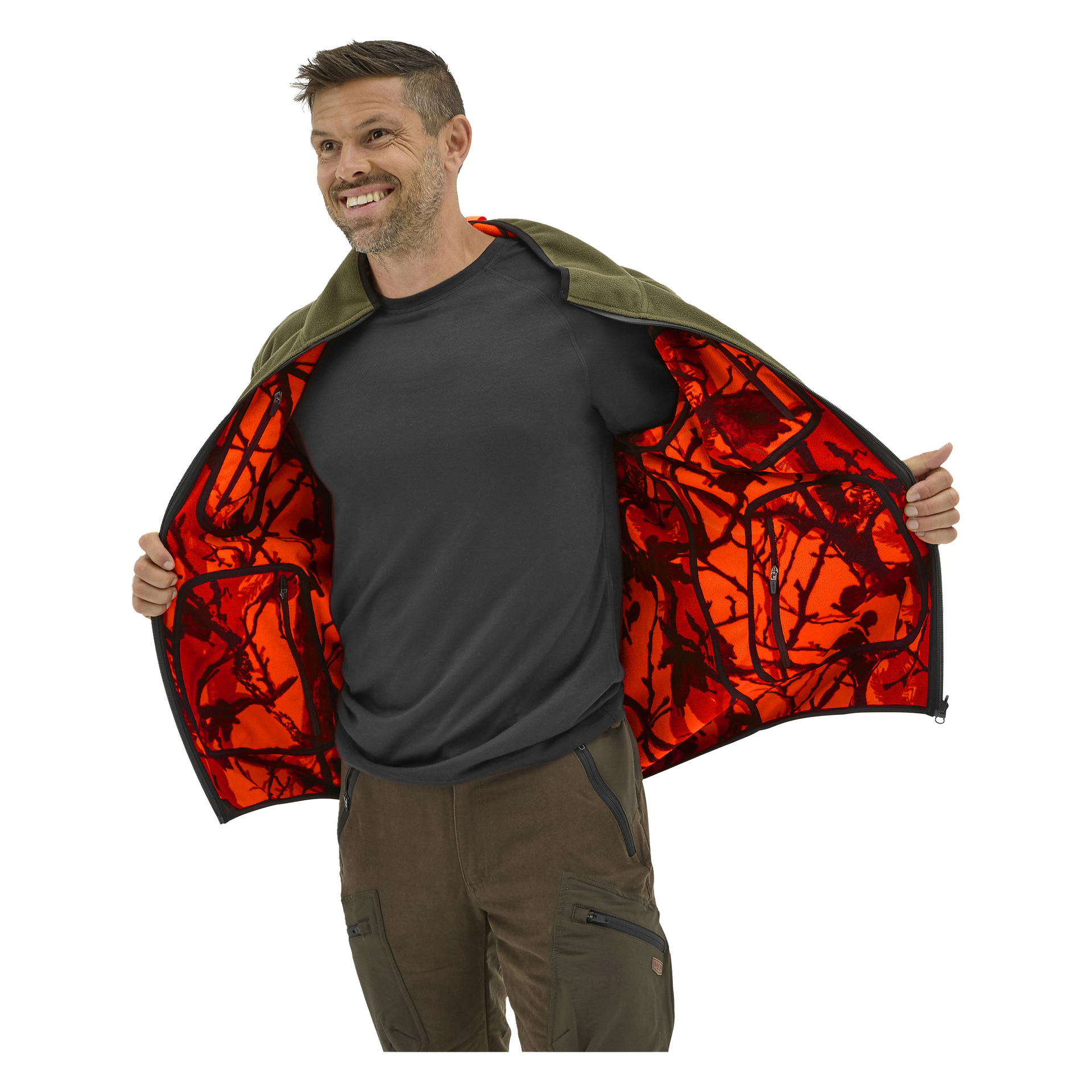 Den leende mannen öppnar en olivfärgad Kayoba-fleecejacka och avslöjar orange kamouflagefoder, som bärs över en svart t-shirt och bruna byxor med dragkedja.