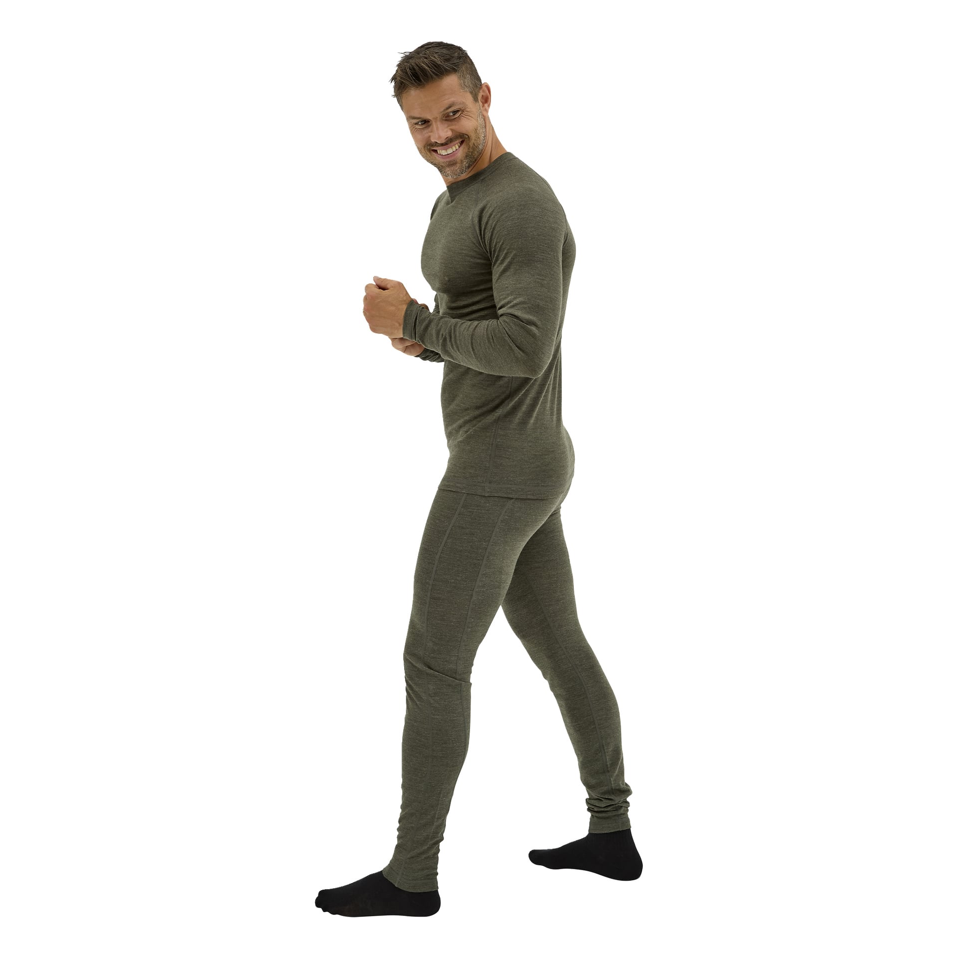 En leende man med kort hår och skägg visar upp ett tvådelat olivgrönt Kayoba Outdoor Merino-ullunderställe, stående på sidan i svarta strumpor.
