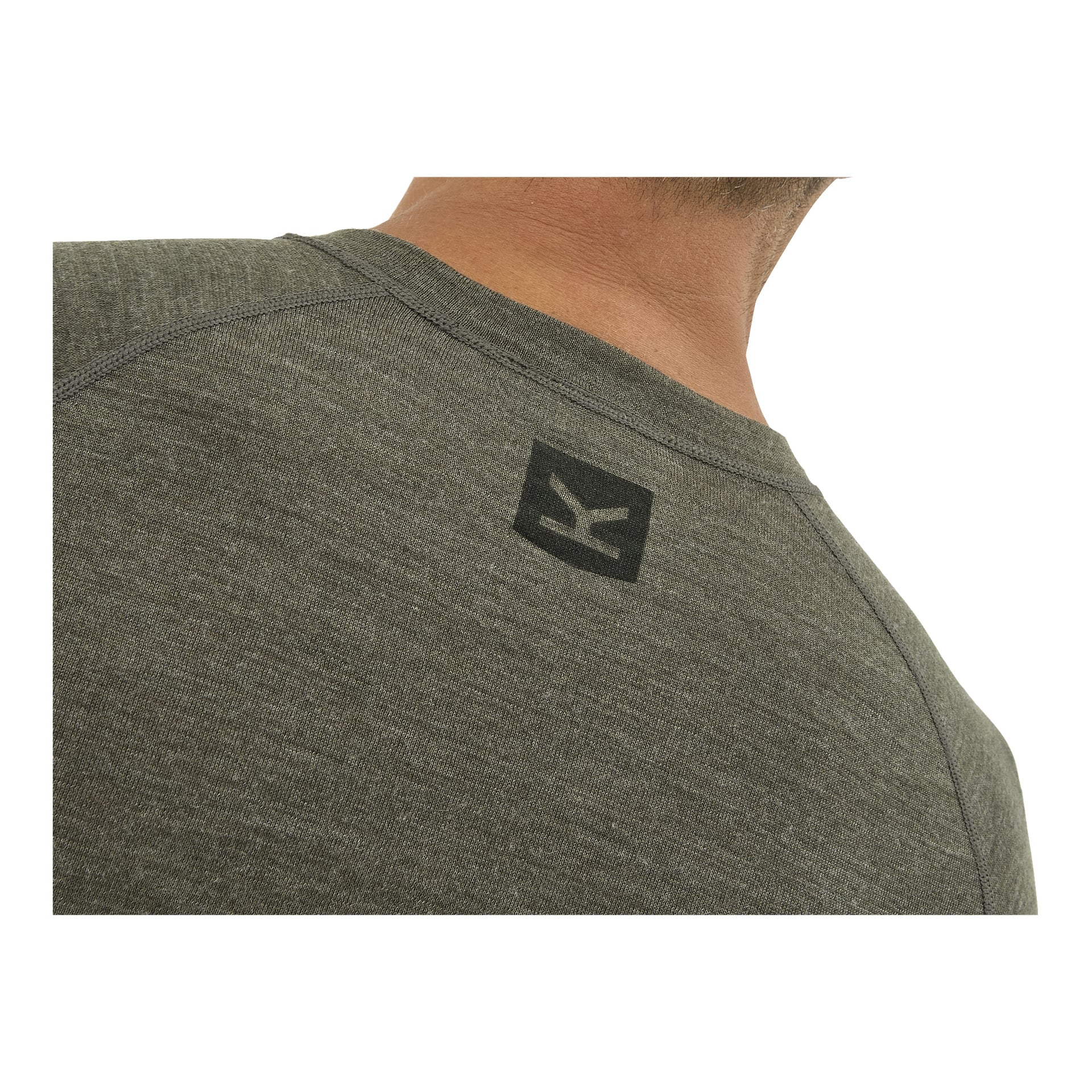 En mans nacke och axel i ett ljungerat grönt Kayoba Outdoor Merino-ullbaslager, med en liten svart geometrisk logga vid kragen.