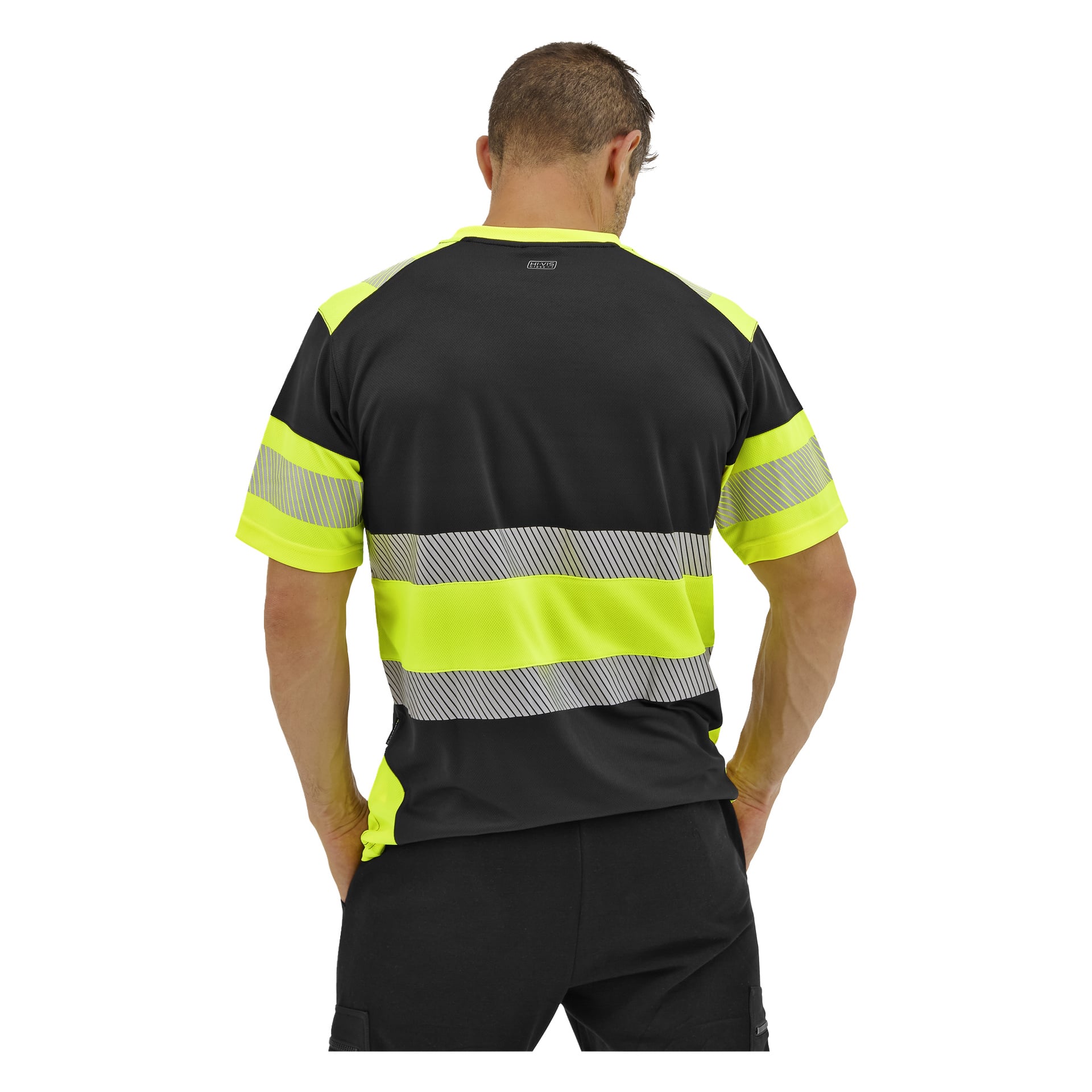 En man står med ryggen mot kameran, klädd i en Bluewear högärmad kortärmad tröja med gula och grå reflekterande ränder och svarta byxor, händerna på höfterna.