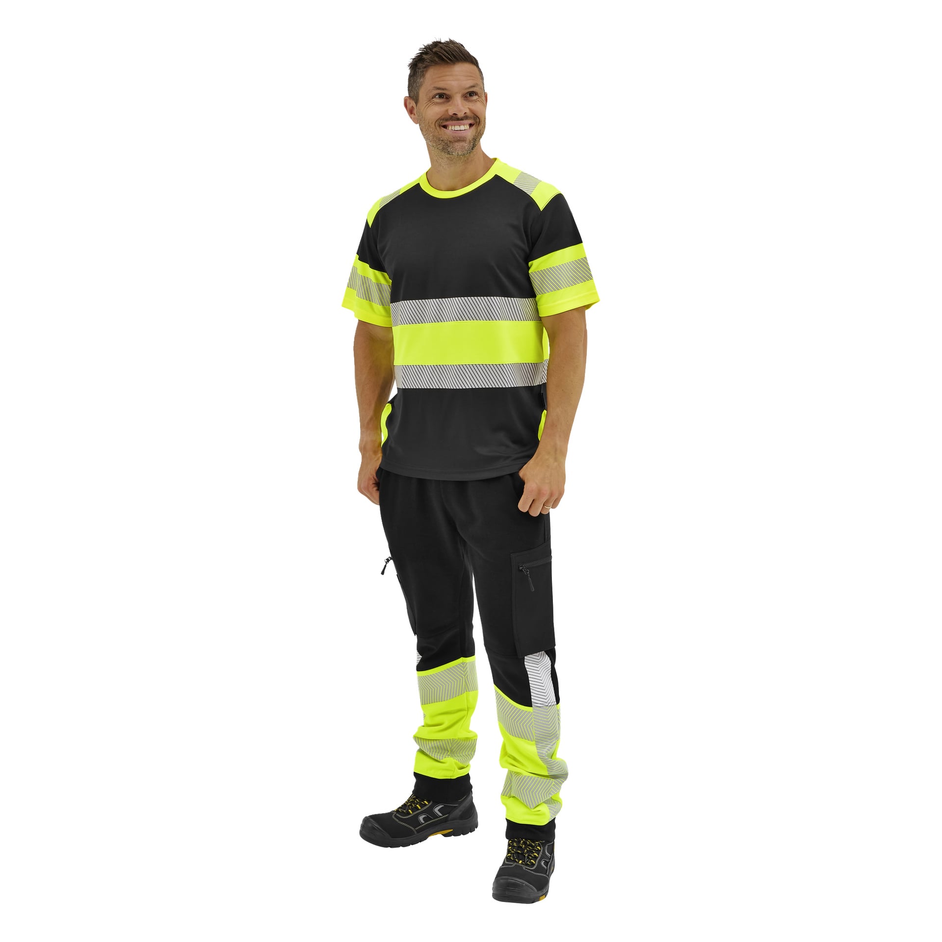 En man i en Bluewear kortärmad hög-vis-tröja med reflekterande ränder, svarta cargobyxor och arbetskängor står leende och tittar åt sidan.