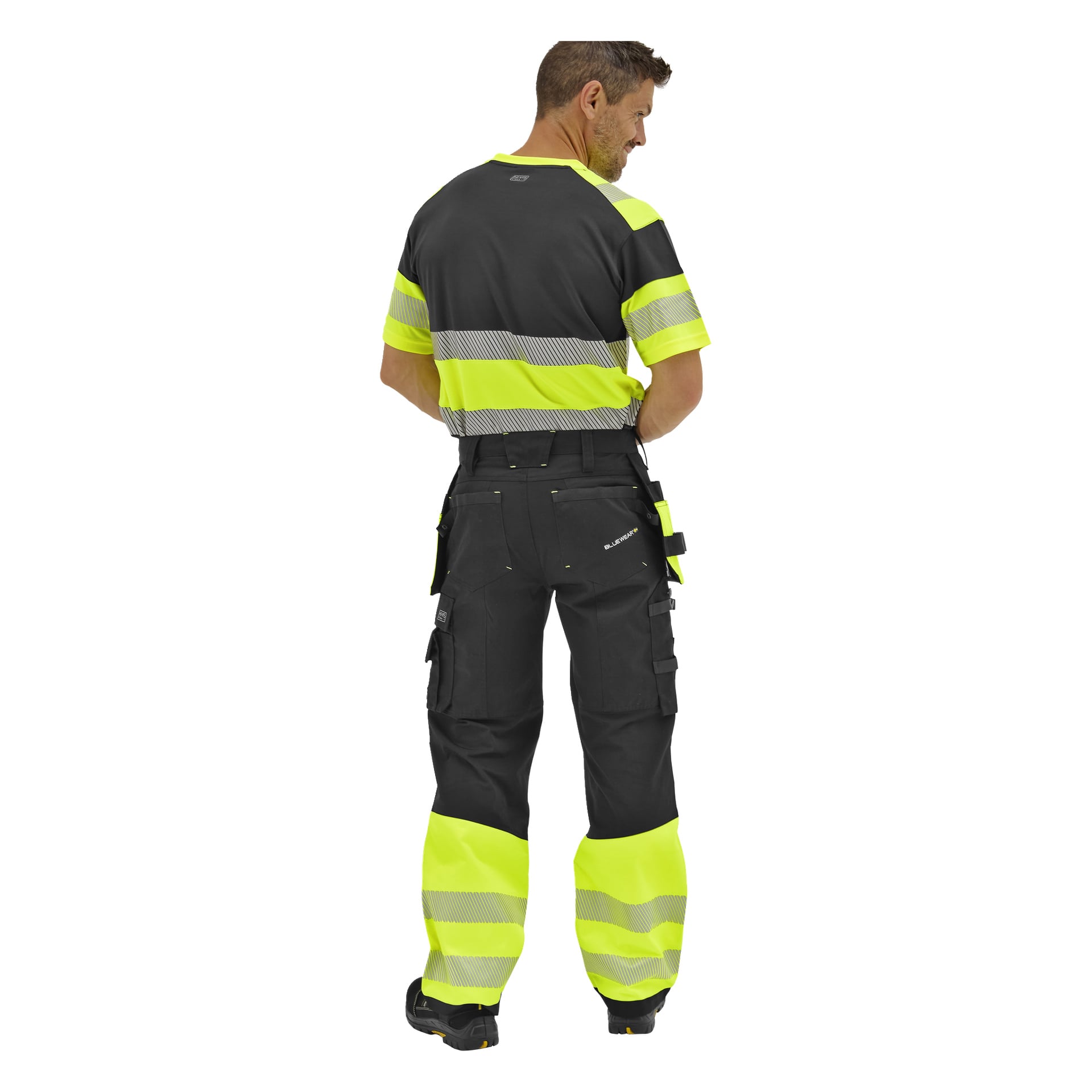 En man som syns bakifrån bär Bluewear Rex högvarselbyxor med limegröna och reflekterande ränder samt en matchande randig t-shirt.