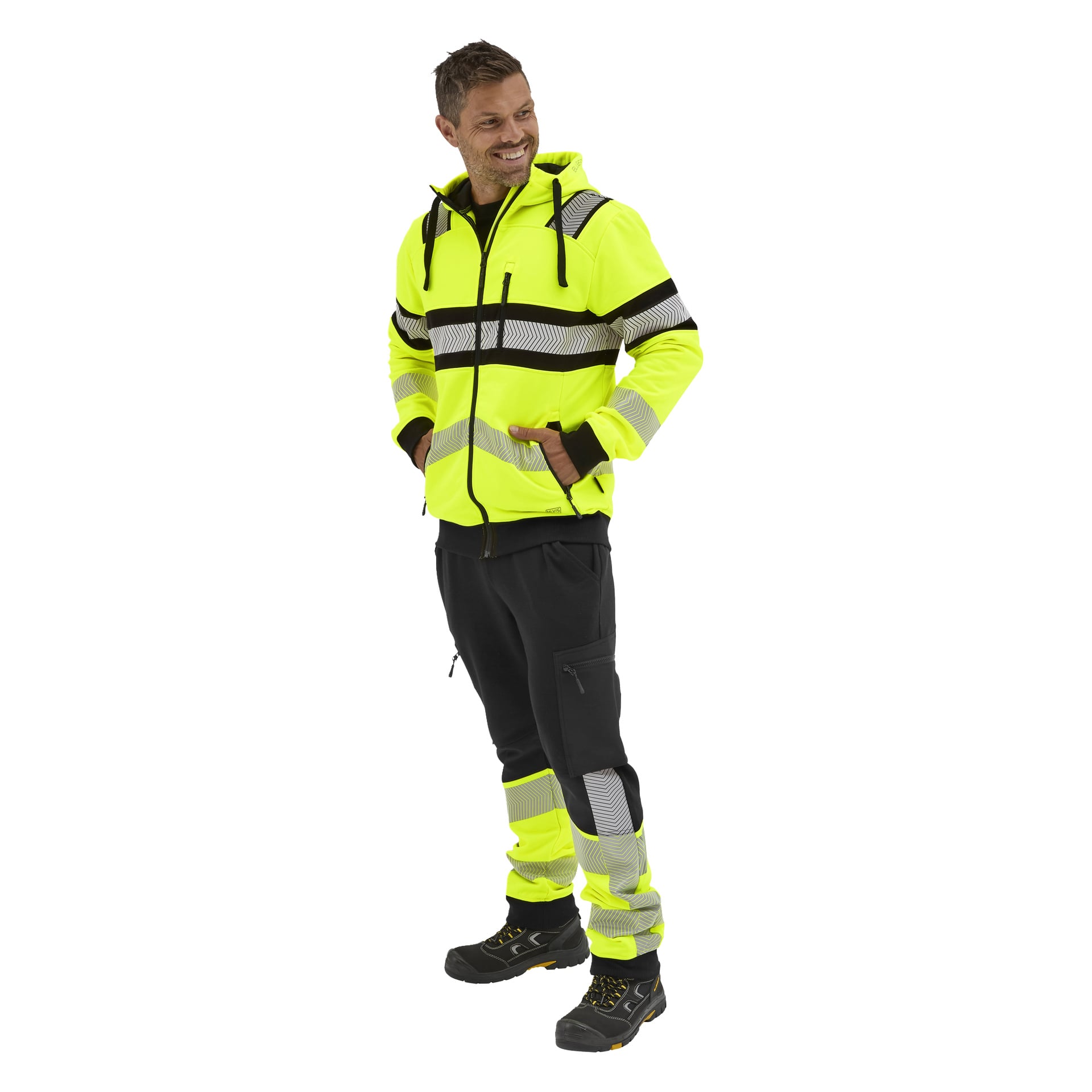 En leende man med händerna i fickorna bär en Bluewear Hi-vis huva, matchande reflexbyxor och svarta arbetsskor.
