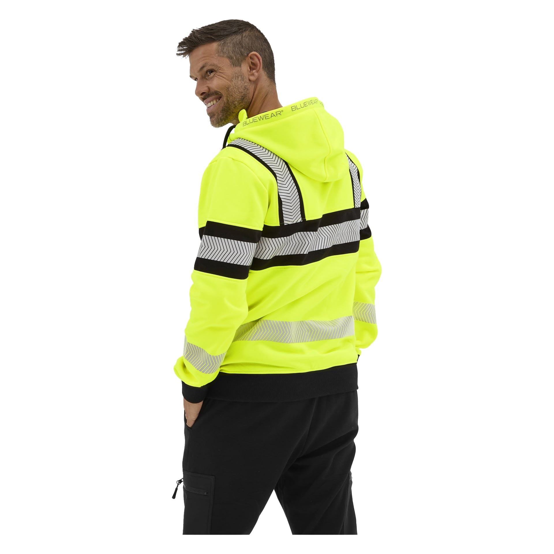 En man, lätt vänd och leende, bär en klargul Bluewear Hi-vis Chambley-hoodie med svarta ränder och chevrons samt svarta byxor.