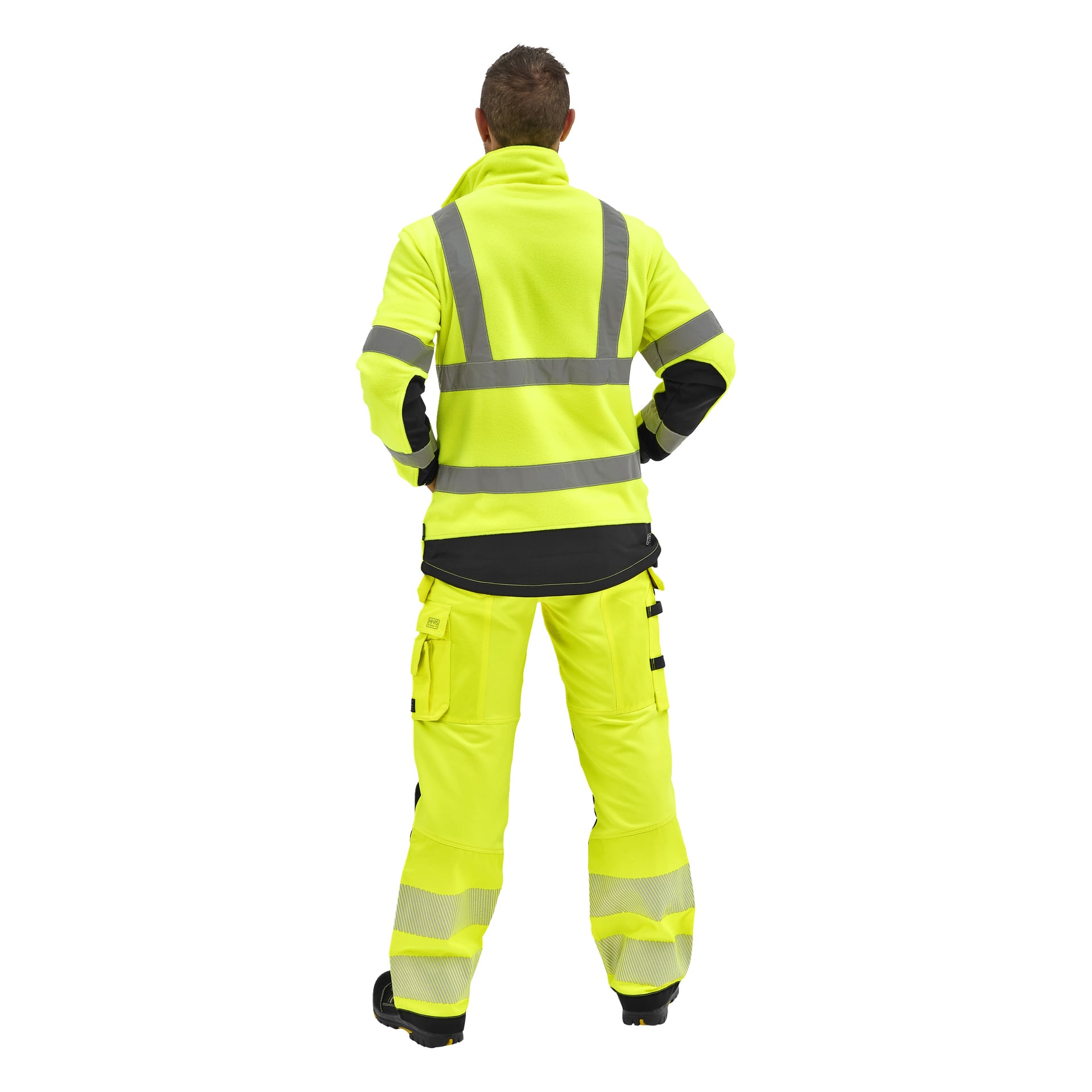 En person står med händerna på höfterna, med ryggen mot kameran, klädd i Bluewear Hi-Vis Chase-jacka och byxor med reflekterande ränder och svarta skor.