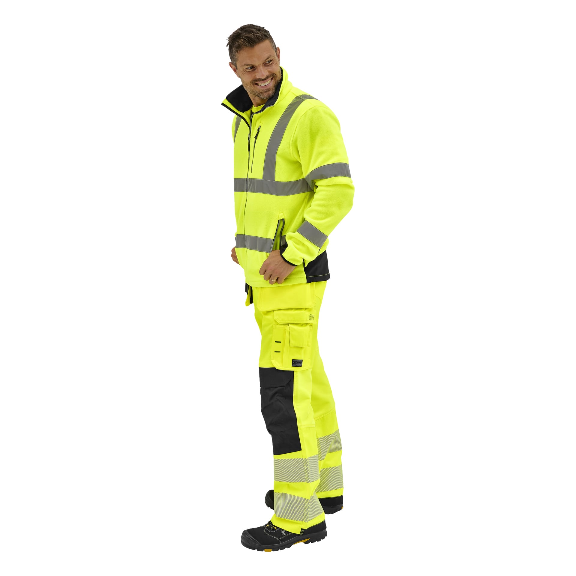 Leende man i Bluewear Hi-Vis fleecejacka Chase och matchande reflekterande byxor, svarta skor, kastar en blick över axeln.