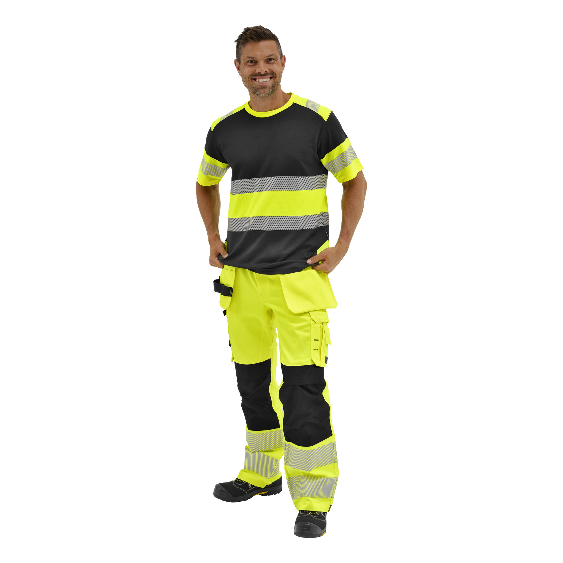 En person i Bluewears Rex-byxor med hög synlighet och reflekterande ränder står leende, ena handen avslappnat i fickan.