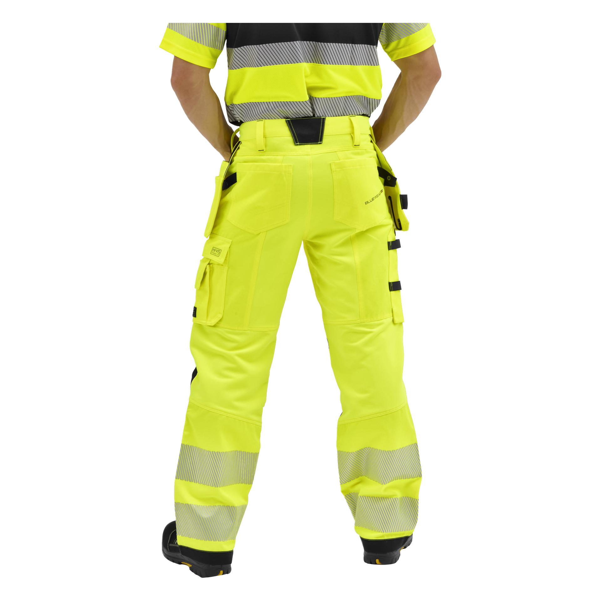 Personen vänd bort, klädd i Bluewear Rex hög-vis-gula byxor med reflekterande ränder, svarta detaljer och många fickor. Överkroppen delvis synlig.
