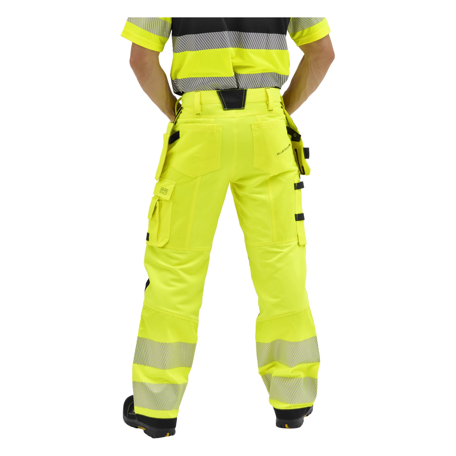 En person vänder sig bort, klädd i Bluewear High Visibility Trousers Rex med reflekterande remsor och svarta detaljer, samt en matchande skjorta.