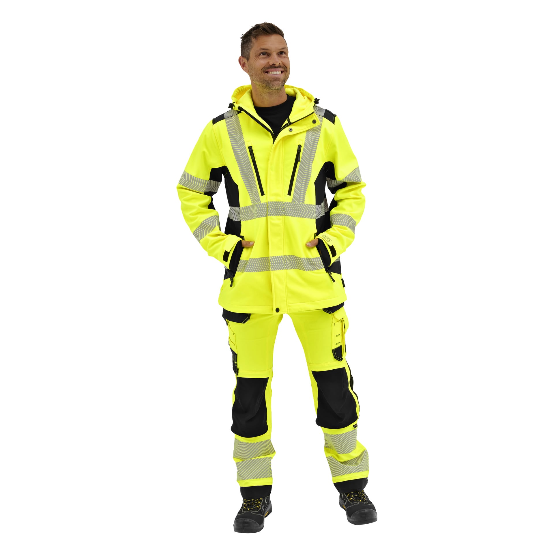 En person som bär en Bluewear Hi-Vis Kingston-softshelljacka med reflekterande ränder, händerna i fickorna, ler när hen tittar upp.