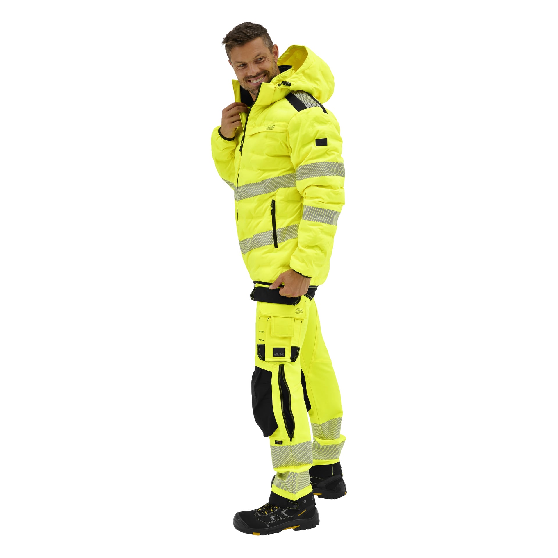 En man bär den gula Bluewear Pro högvarseljackan Jasper med svarta detaljer, reflekterande ränder, matchande byxor och arbetsstövlar.