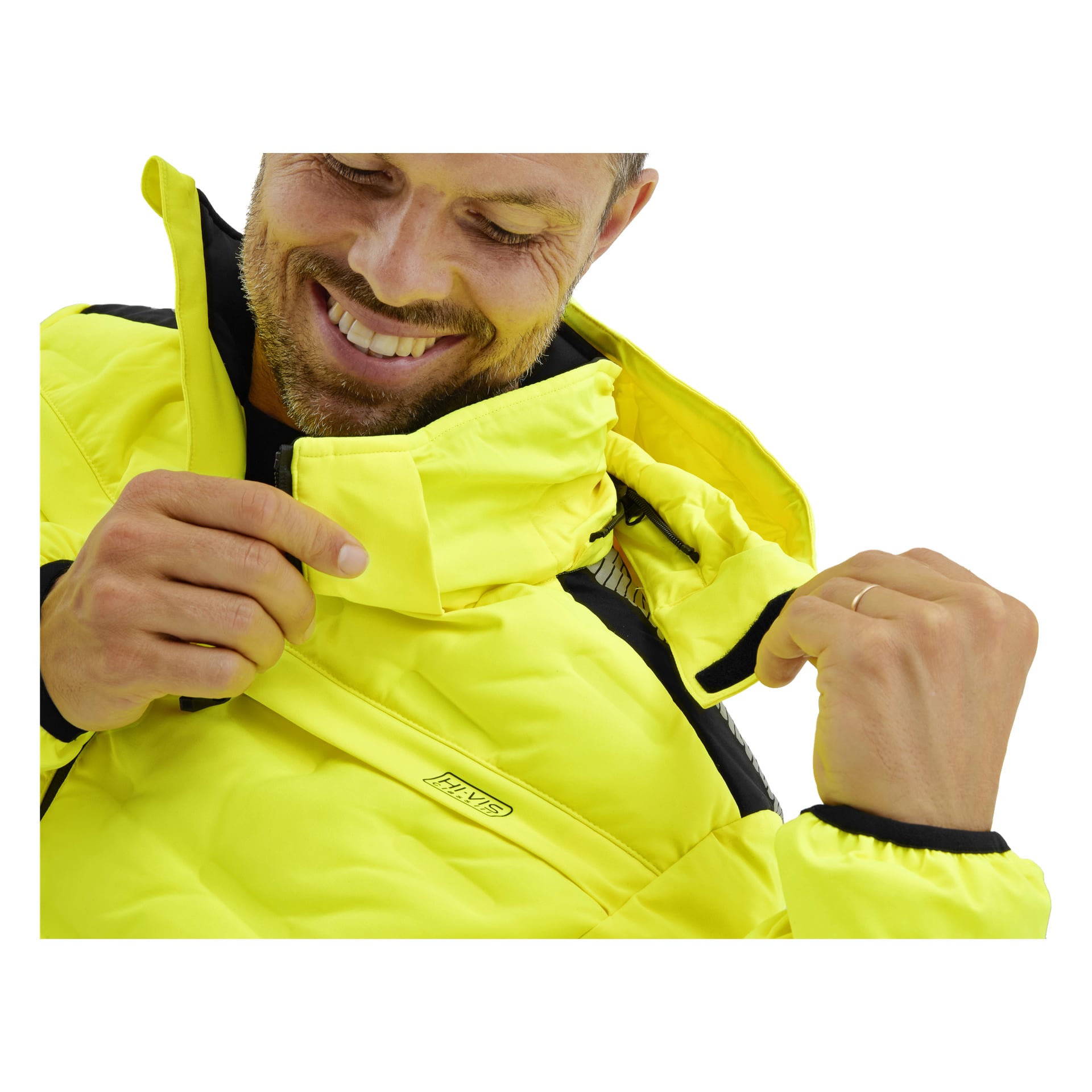 En man ler och visar tänderna, medan han justerar kragen och dragkedjan på en klargul Padded hi-vis Bluewear Pro Workwear-jacka.