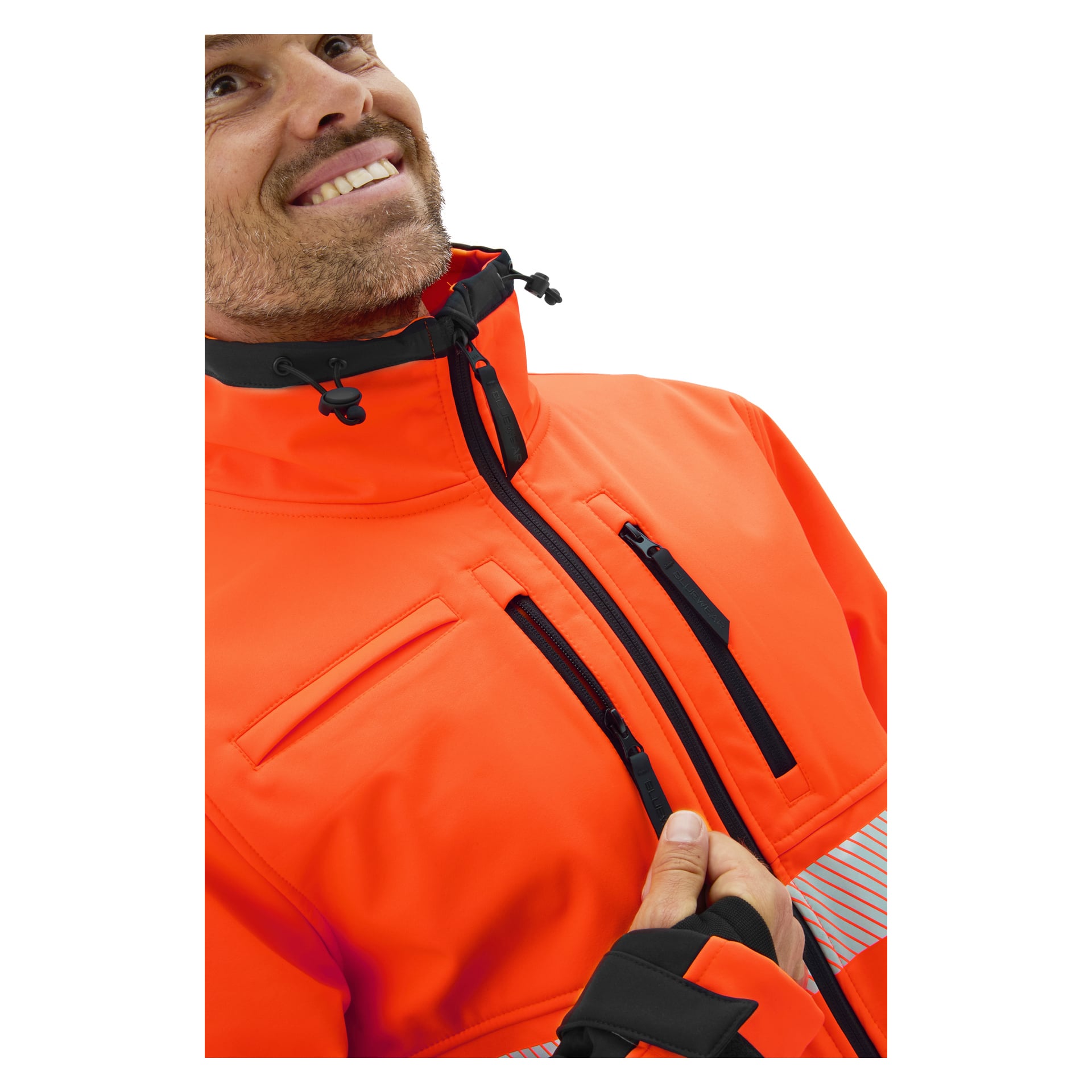 En person ler medan man drar upp en knallorange Bluewear Hi-Vis softshelljacka Toronto med svarta dragkedjor och detaljer.
