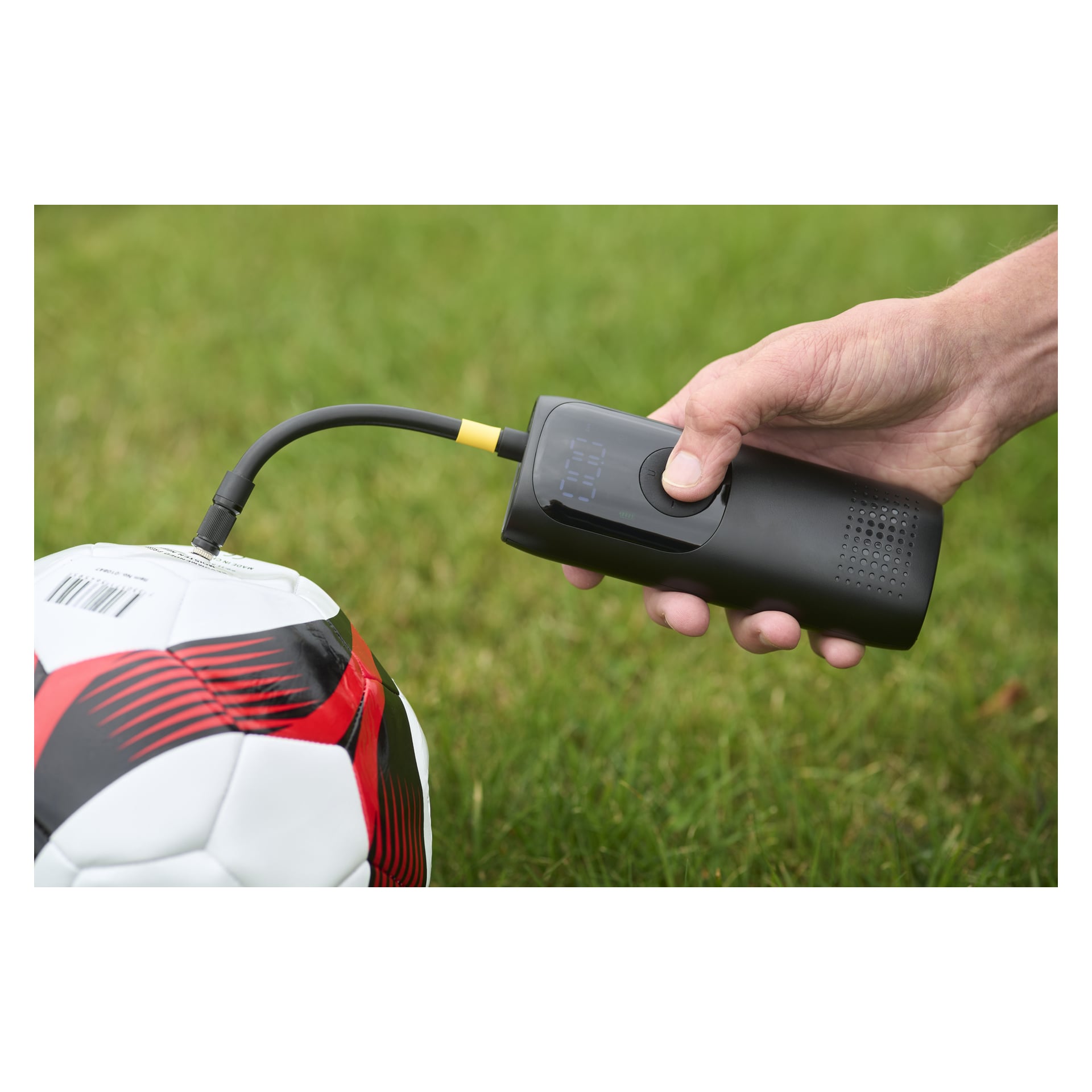 Någon blåser upp en röd, svart och vit fotboll på gräset med hjälp av en Hamron Portable-däckpump med digital skärm.