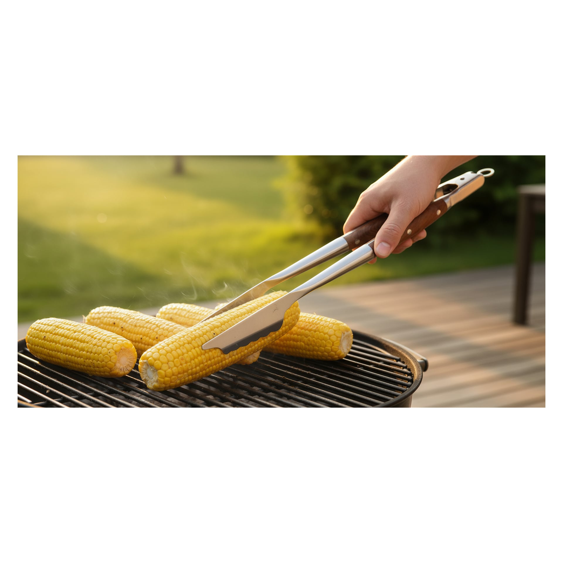 En hand vrider en majskolv med Burns & Barkles-tång medan fyra kolben ångar på en kolgrill, solljuset lyser upp gräsmattan bakom.