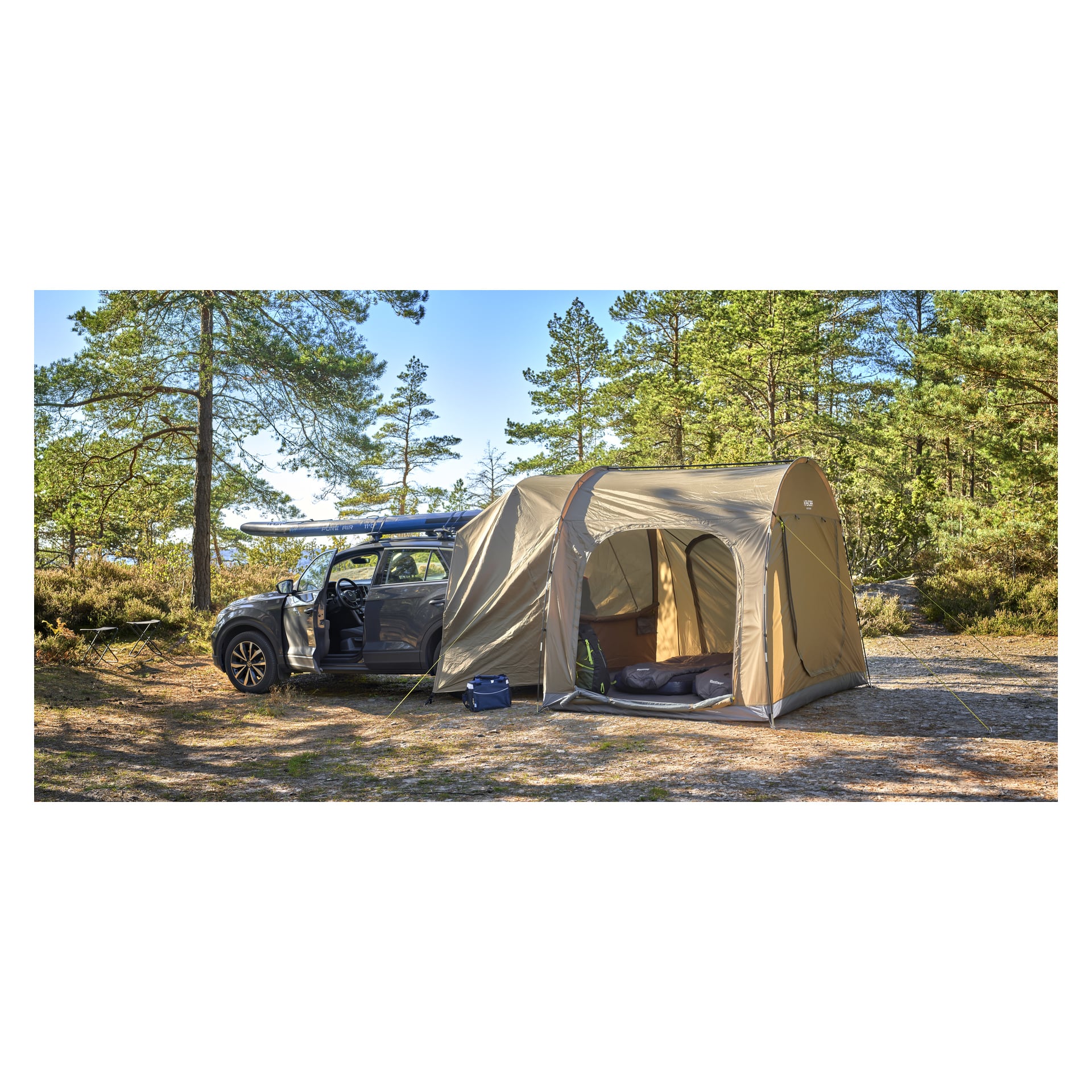 Grå SUV i en skogsglänta med ett beige tält på sidan, paddleboards på taket och campingutrustning uppställd i närheten.