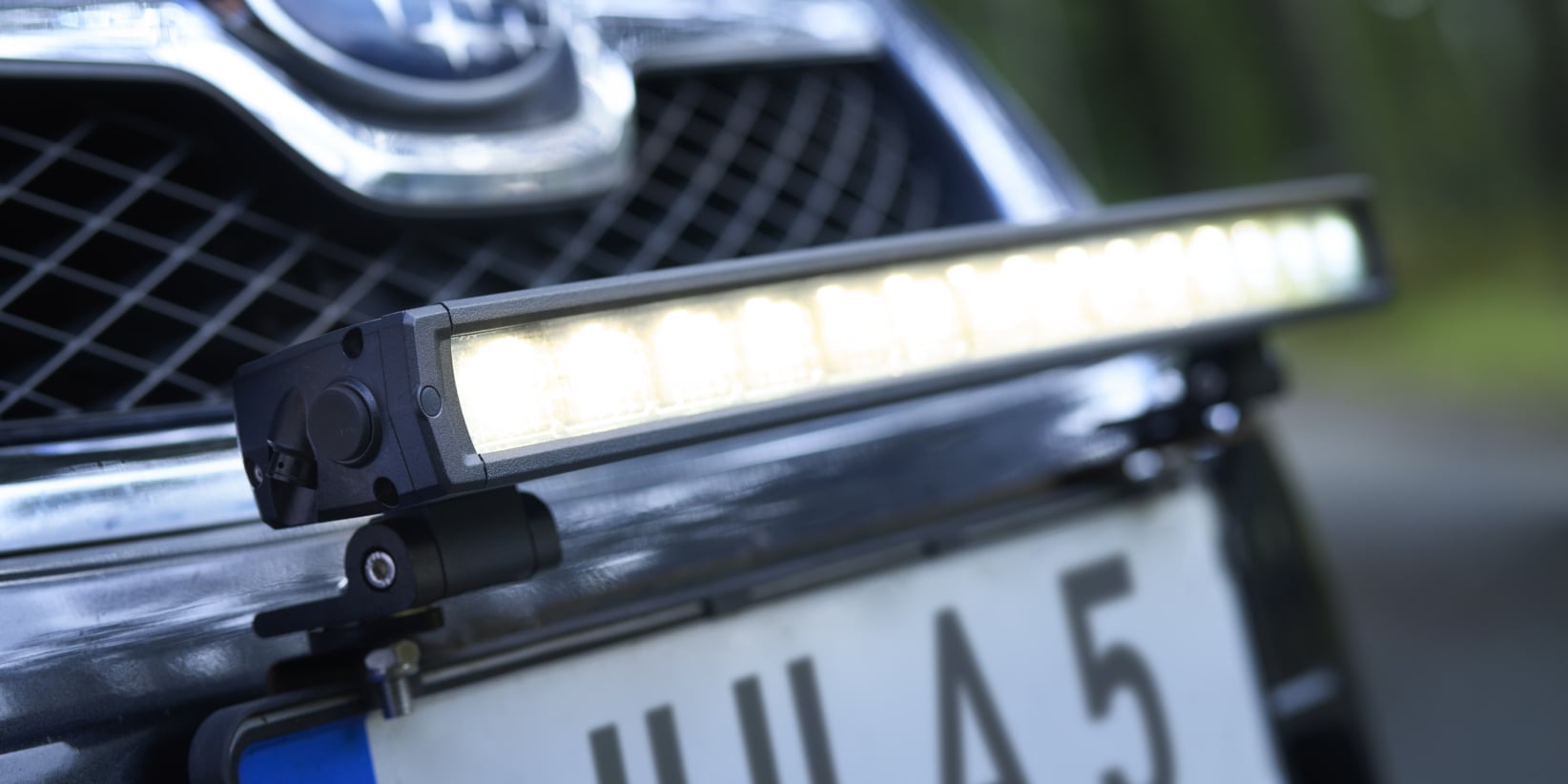 Närbild av en bils frontgrill med ett Subaru-emblem, en registreringsskylt i europeisk stil med texten "JLA 5" och en monterad LED-ljusramp som tänds ovanför skylten.