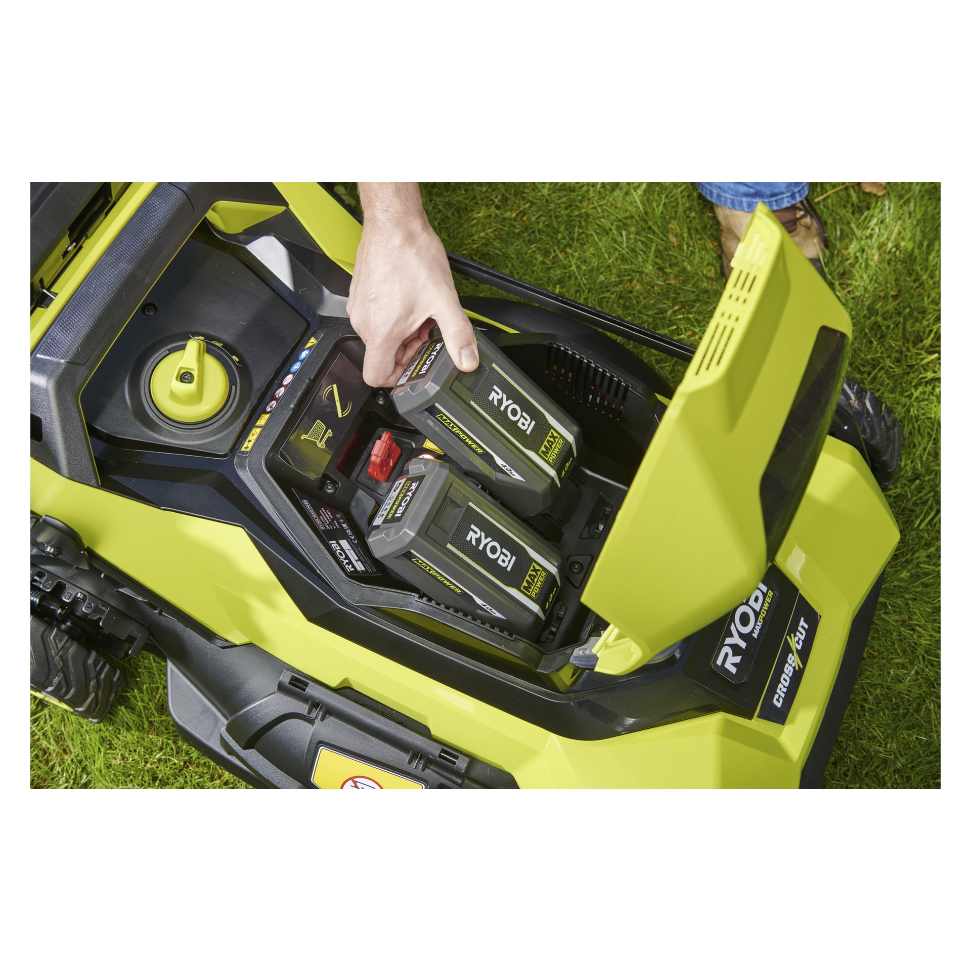 Någon placerar ett Ryobi 40V-batteri i RY36LMXSP53B-160-gräsklipparen på gräset, vilket visar två platser under det öppna gröna locket.