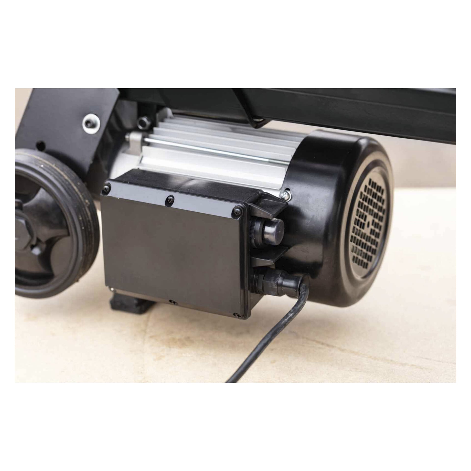 Närbild på Scheppach Log Splitter BLS7L Black Edition-motorn med svart lock, ledningar och delar av mekanismen på beige yta.