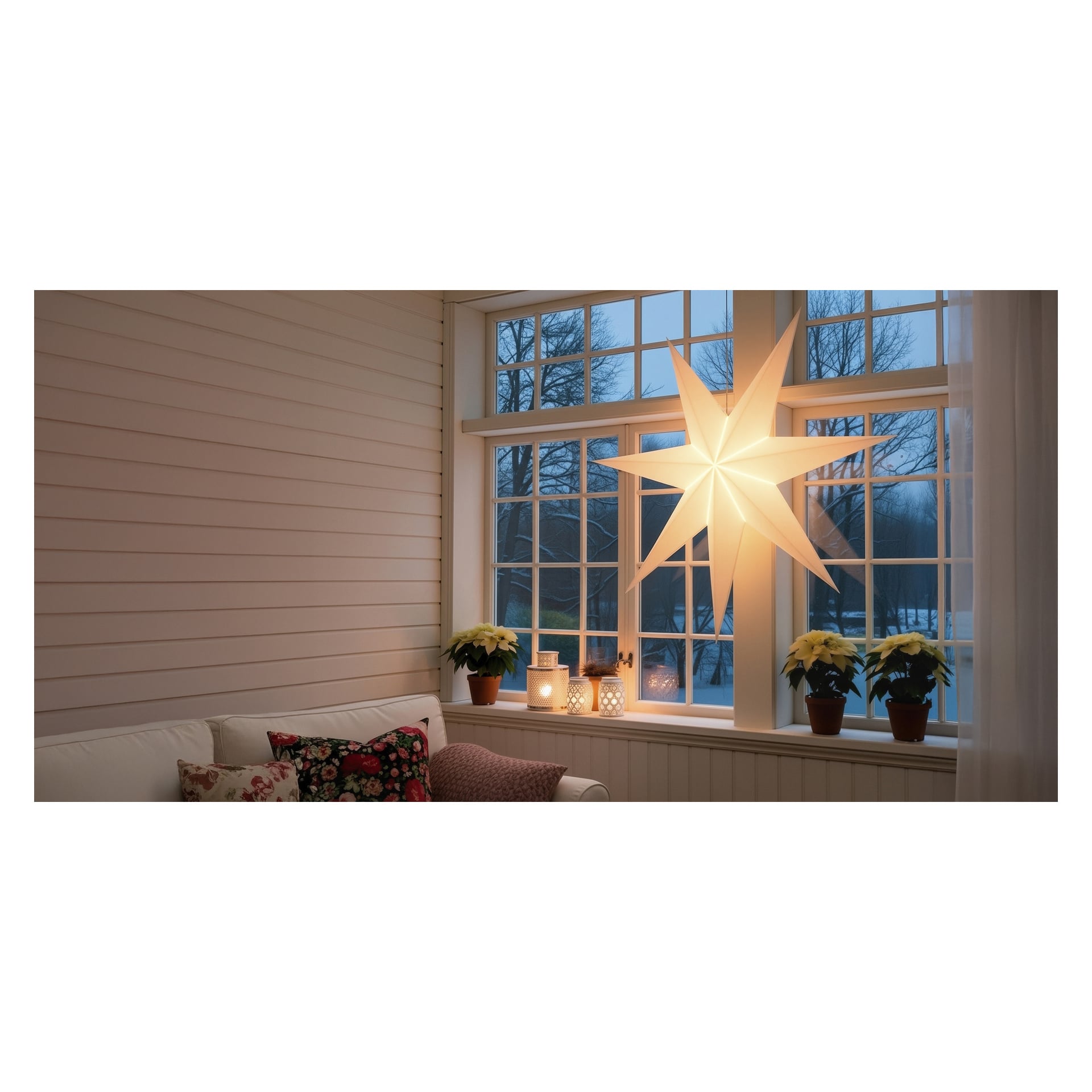 EKVIP White Advent -tähti roikkuu ikkunalaudalla ikkunalaudalla, joka on koristeltu ruukkujoulutähdillä ja kynttilöillä." Ulkona näkyy puita ja lunta, ja etualalla on valkoinen sohva kukkatyynyineen.