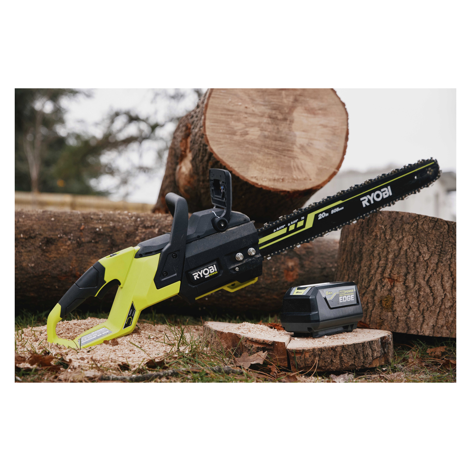 Ryobi sladdlös motorsåg på sågade stockar utanför, med sitt batteri nära; fler stockar och suddiga träd i bakgrunden.