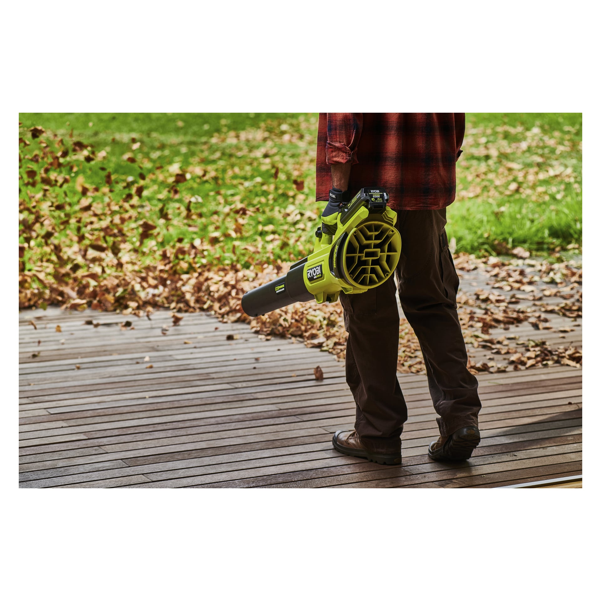 Eine Person auf einem Holzdeck benutzt eine limonengrüne Ryobi Max Power Battery RY36BET40A Laubbläser, um heruntergefallene Blätter zu entfernen.
