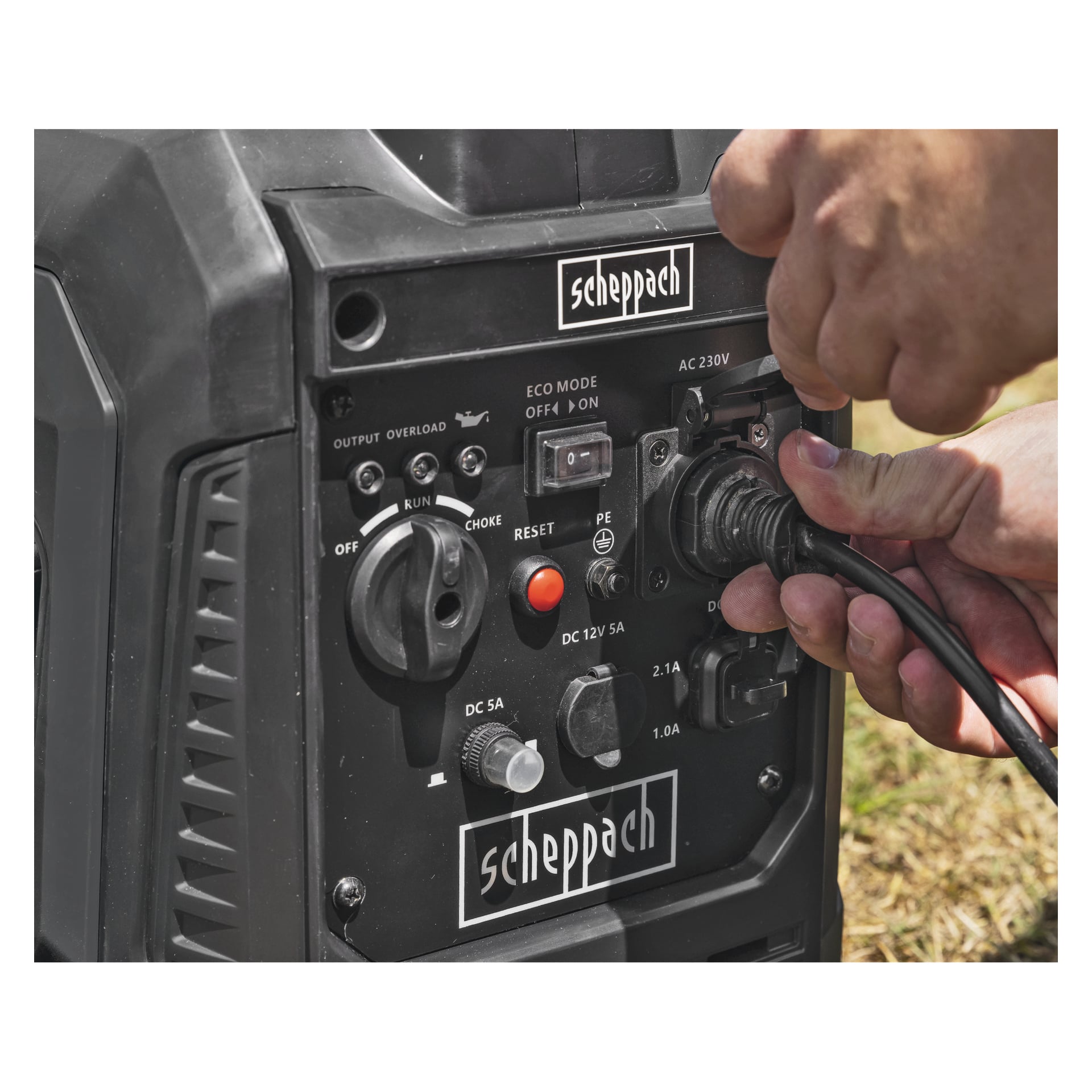 En hand ansluter en kabel till kontrollpanelen på en svart Scheppach-generator med synliga strömbrytare, uttag och indikatorlampor.