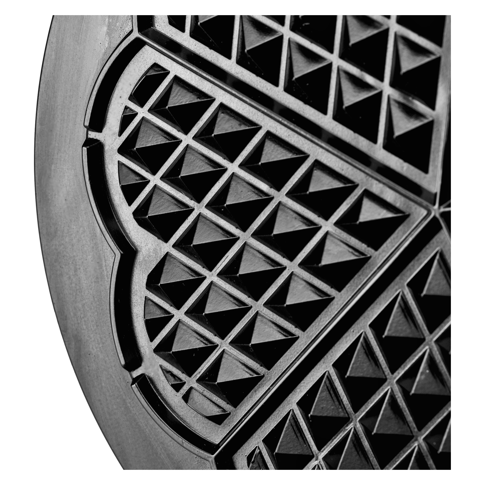 Svart vaffeljernsplate i nærbilde, med hjerteformede design, trekantede rutenett og synlige metallkanter rundt sirkelen.