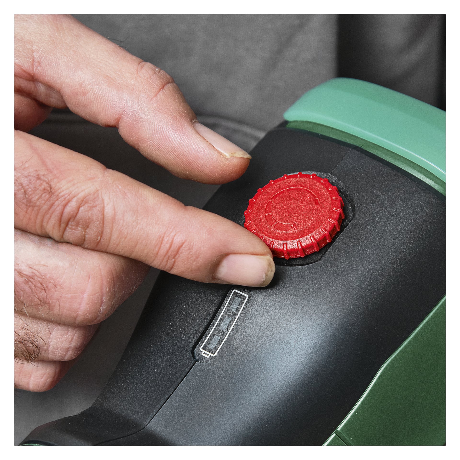 En persons hand vrider en röd urtavla på en svart och grön enhet, med en liten rektangulär LED-indikatorpanel precis under urtavlan.
