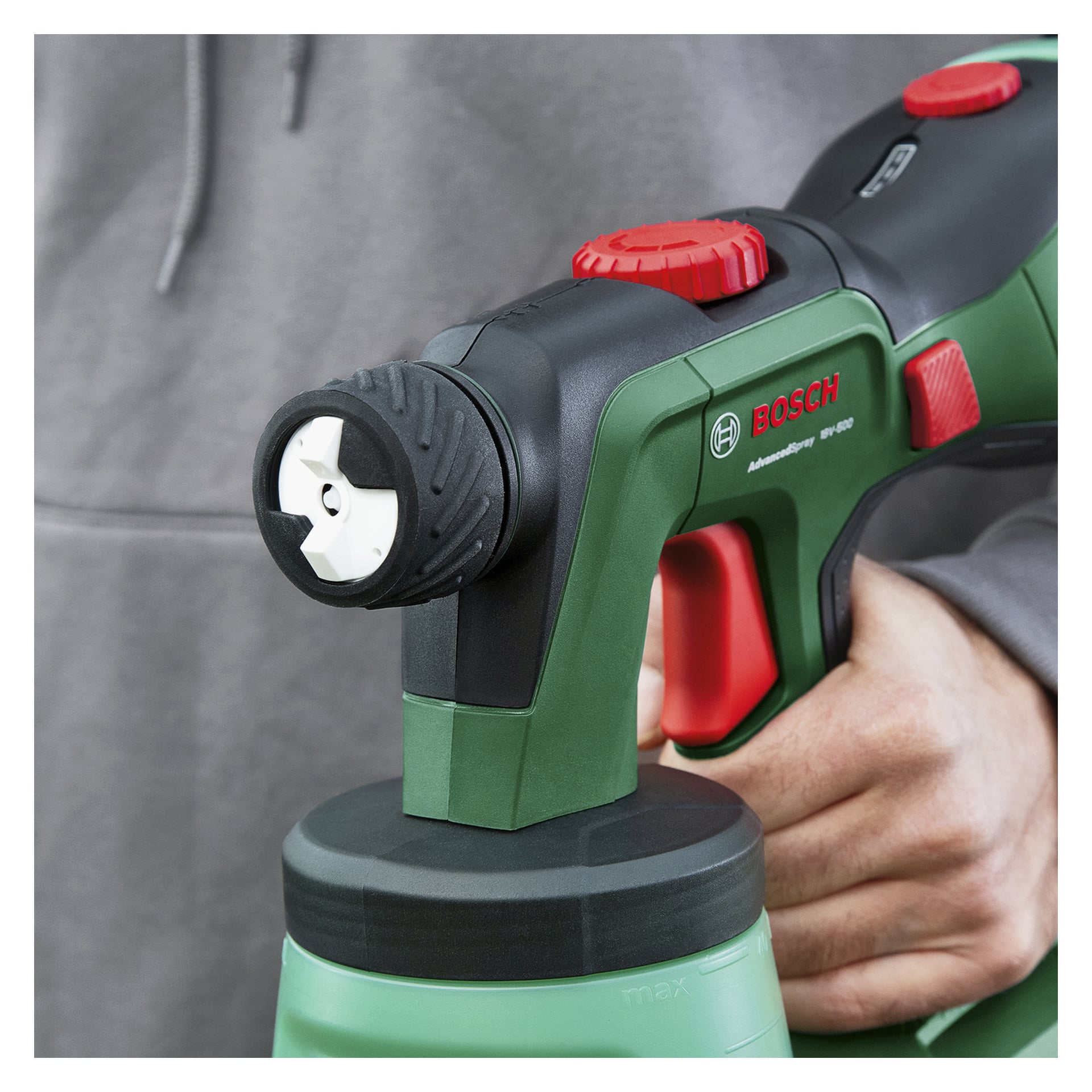 En person håller i en Bosch AdvancedSpray 18V-1000 sprutpistol med en svart och grön kropp, röd avtryckare och basfäst flaska.