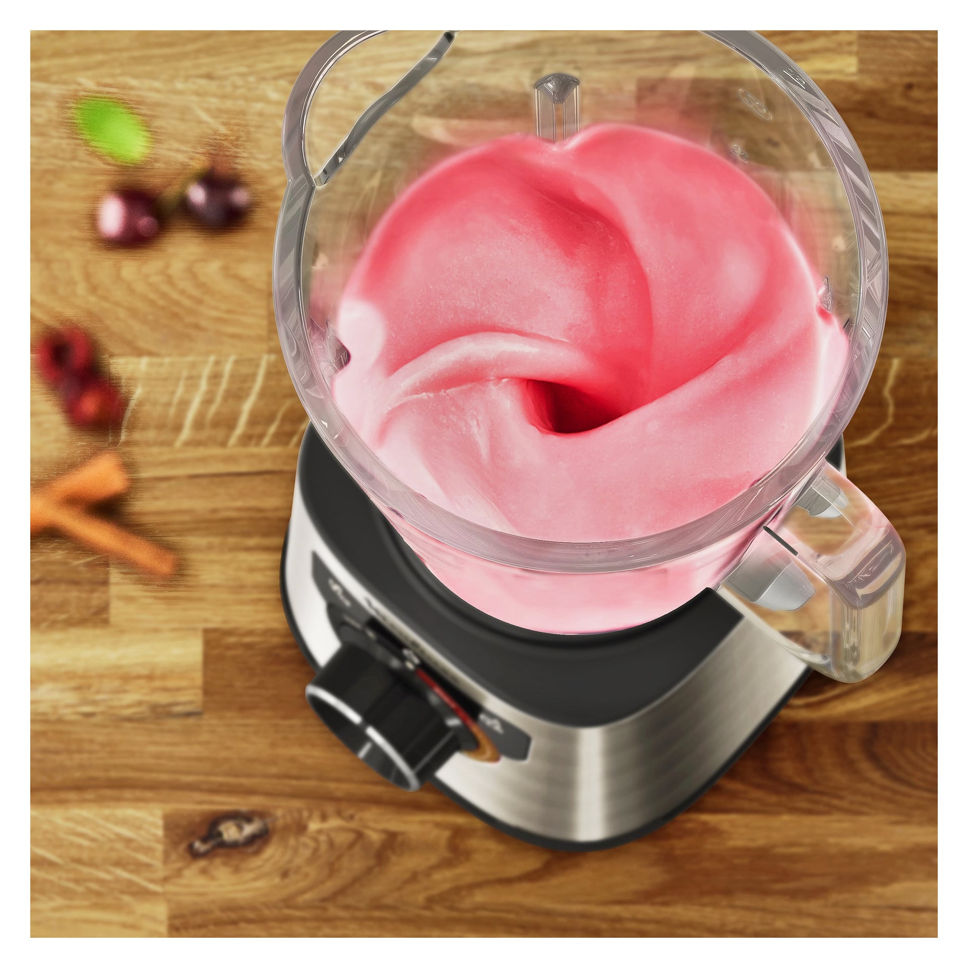 En vy uppifrån och ner visar en mixer på trä som blandar en rosa och vit krämig blandning. Suddiga ingredienser visas i bakgrunden.