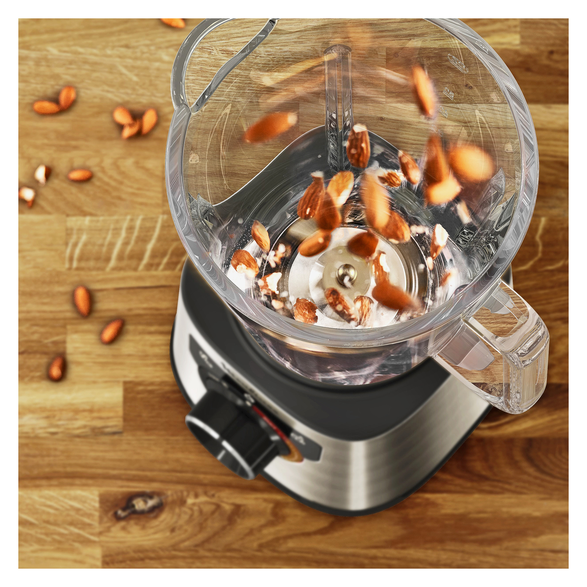 Hackade mandlar hälls i en genomskinlig mixer på en bänkskiva av trä; Mixern har en metallisk bas och svart knopp.