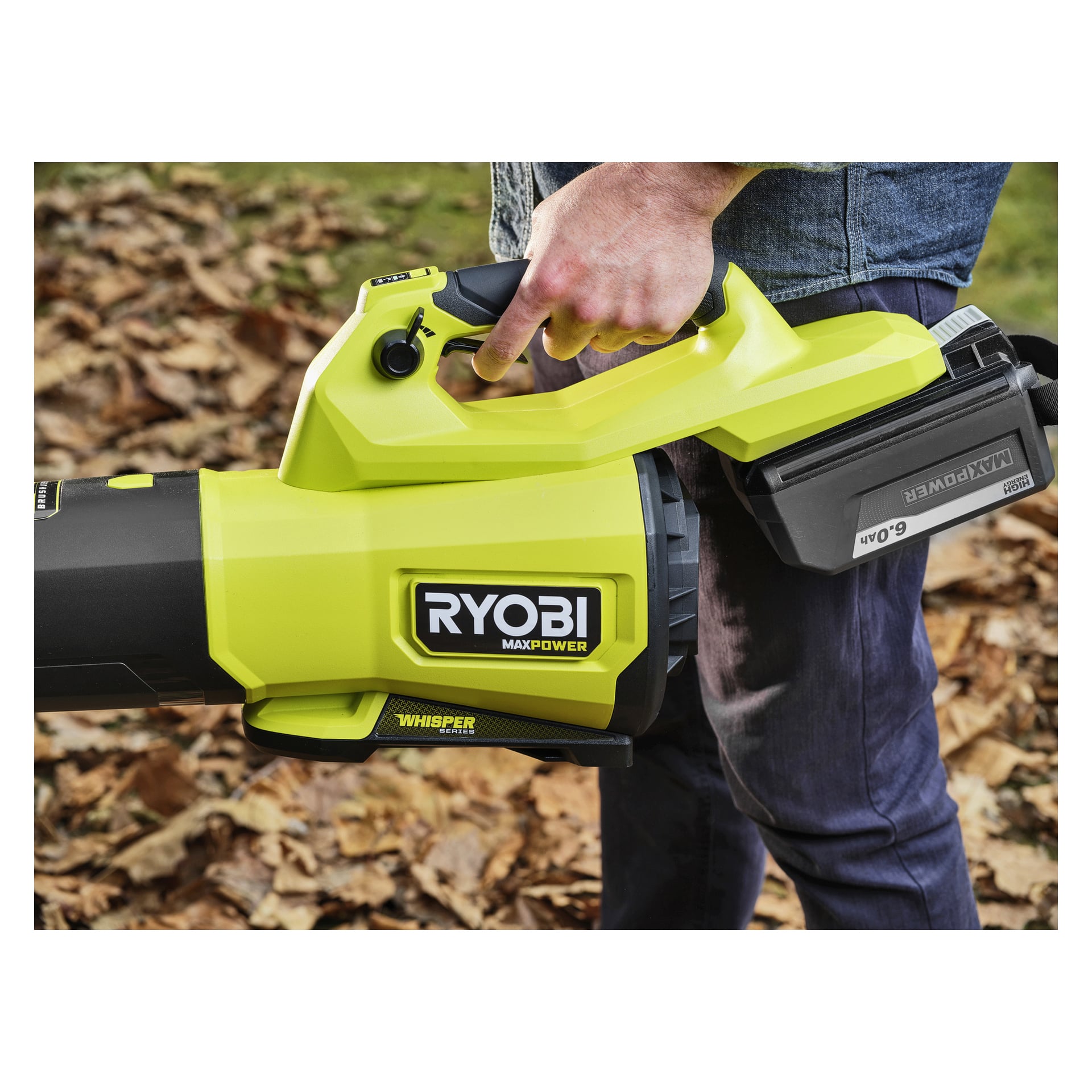 Någon utomhus greppar en Ryobi Max Power sladdlös lövblåsare med ett 6,0 Ah-batteri, torra löv utspridda runt fötterna.